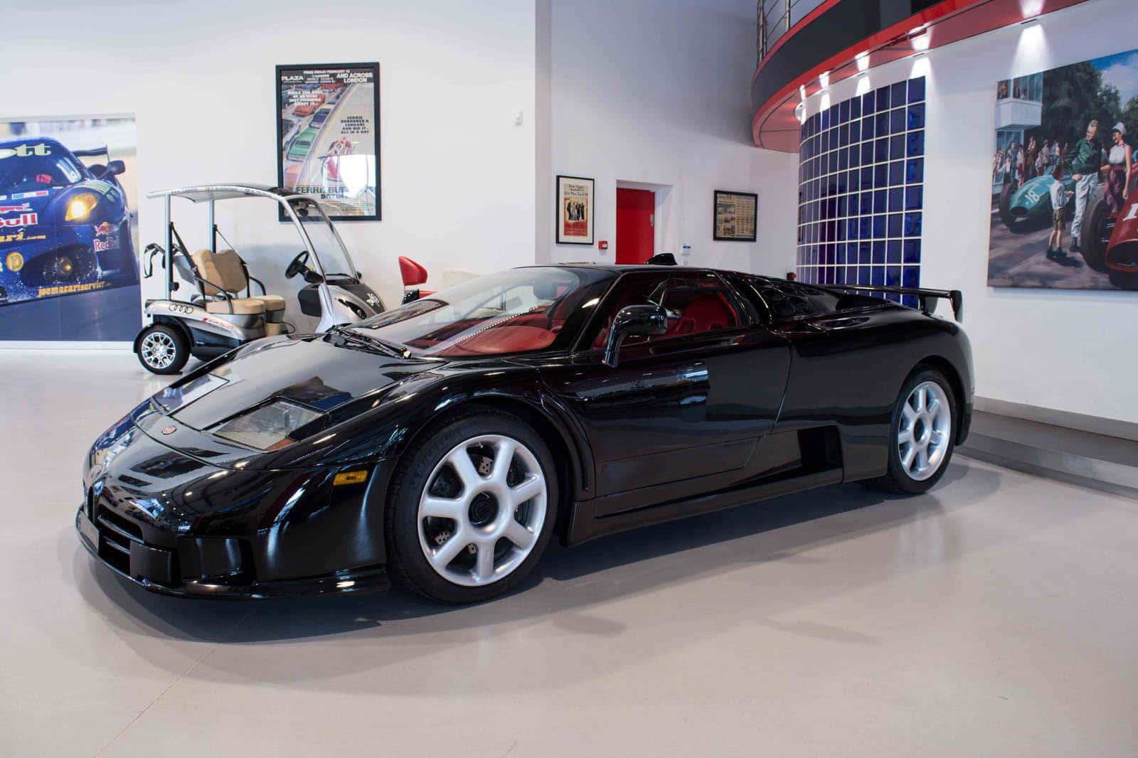 Bugatti Eb110 桌布 壁紙 — 一輛時尚的黑色Bugatti跑車在明亮的燈光下閃閃發光，位於現代汽車展示間內，附近有賽車海報和高爾夫球車。