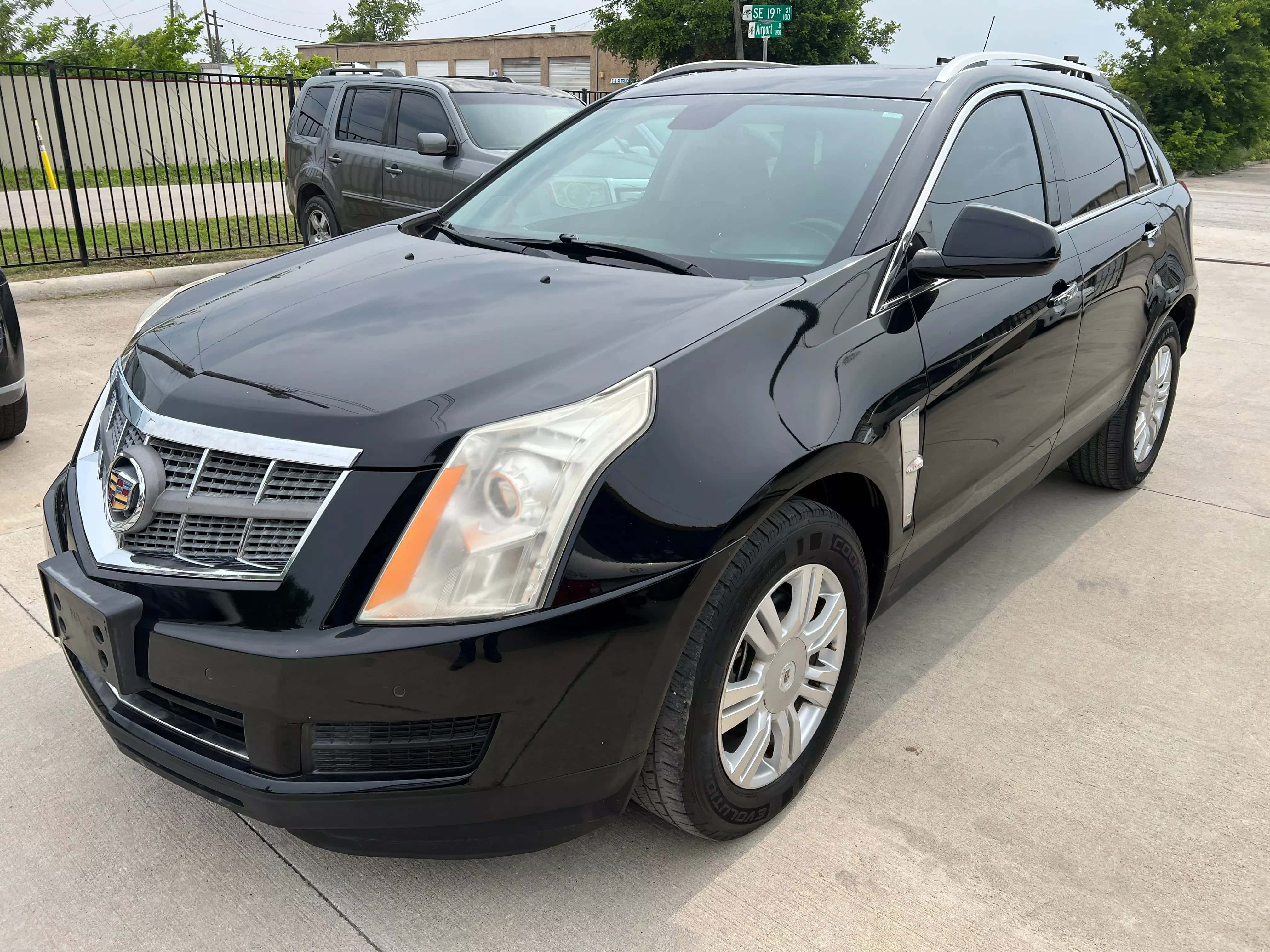 Cadillac Srx 桌布 壁紙 — 一輛時尚的黑色 Cadillac SRX SUV 停放在混凝土停車場，背景有樹木和圍欄。