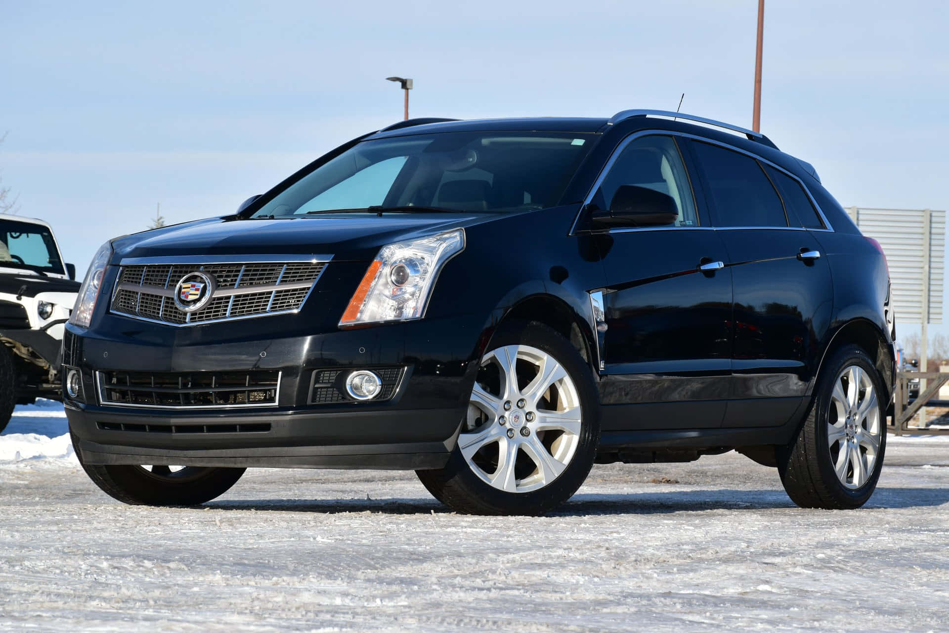 Cadillac Srx 桌布 壁紙 — 一輛時尚的黑色Cadillac SRX SUV停放在雪地上，天空清澈湛藍，陽光在其拋光表面反射。