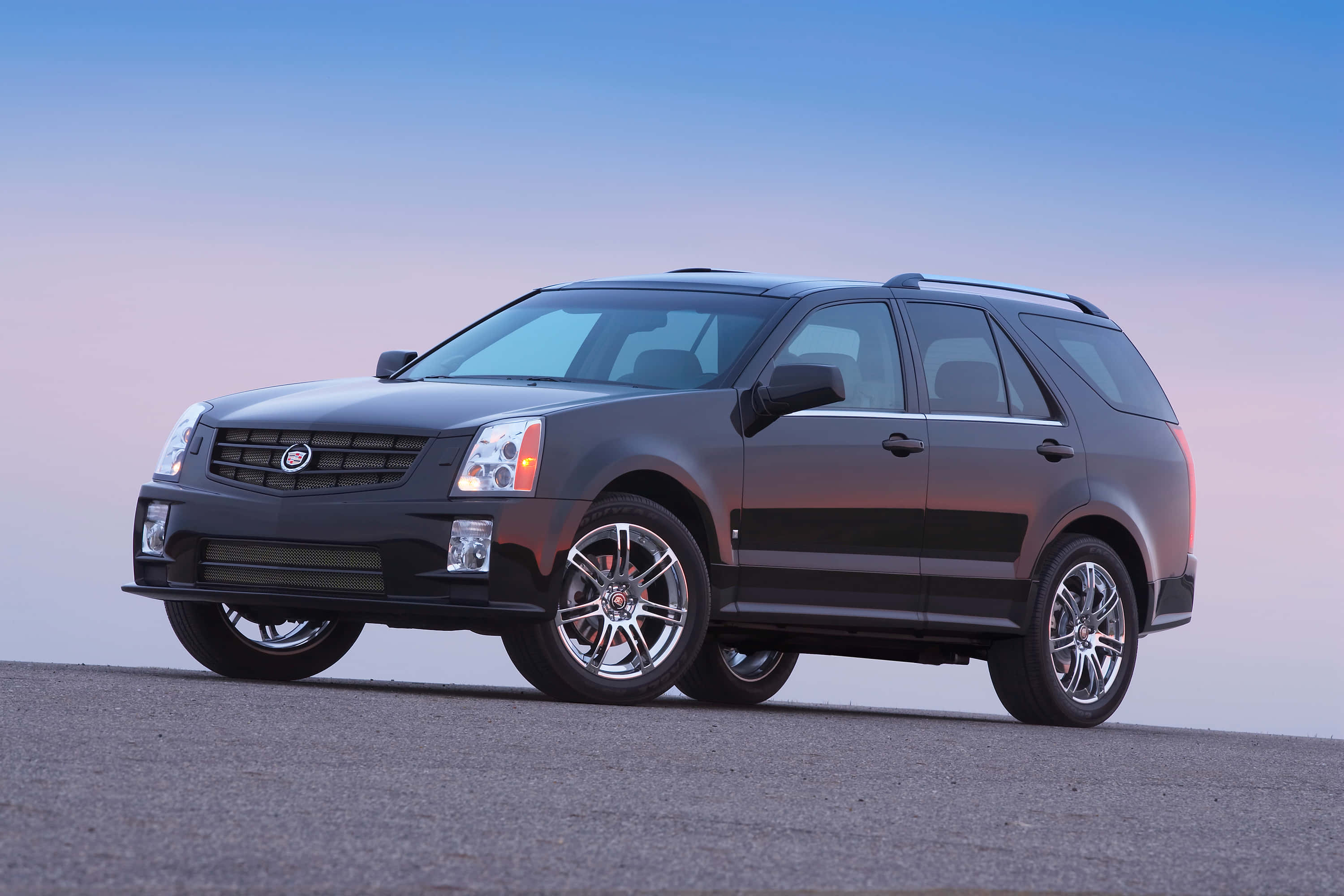 Cadillac Srx 桌布 壁紙 — 一輛時尚的黑色Cadillac SUV停在柏油路上，背景是柔和暮色天空，帶有漸層藍色和粉紅色調。