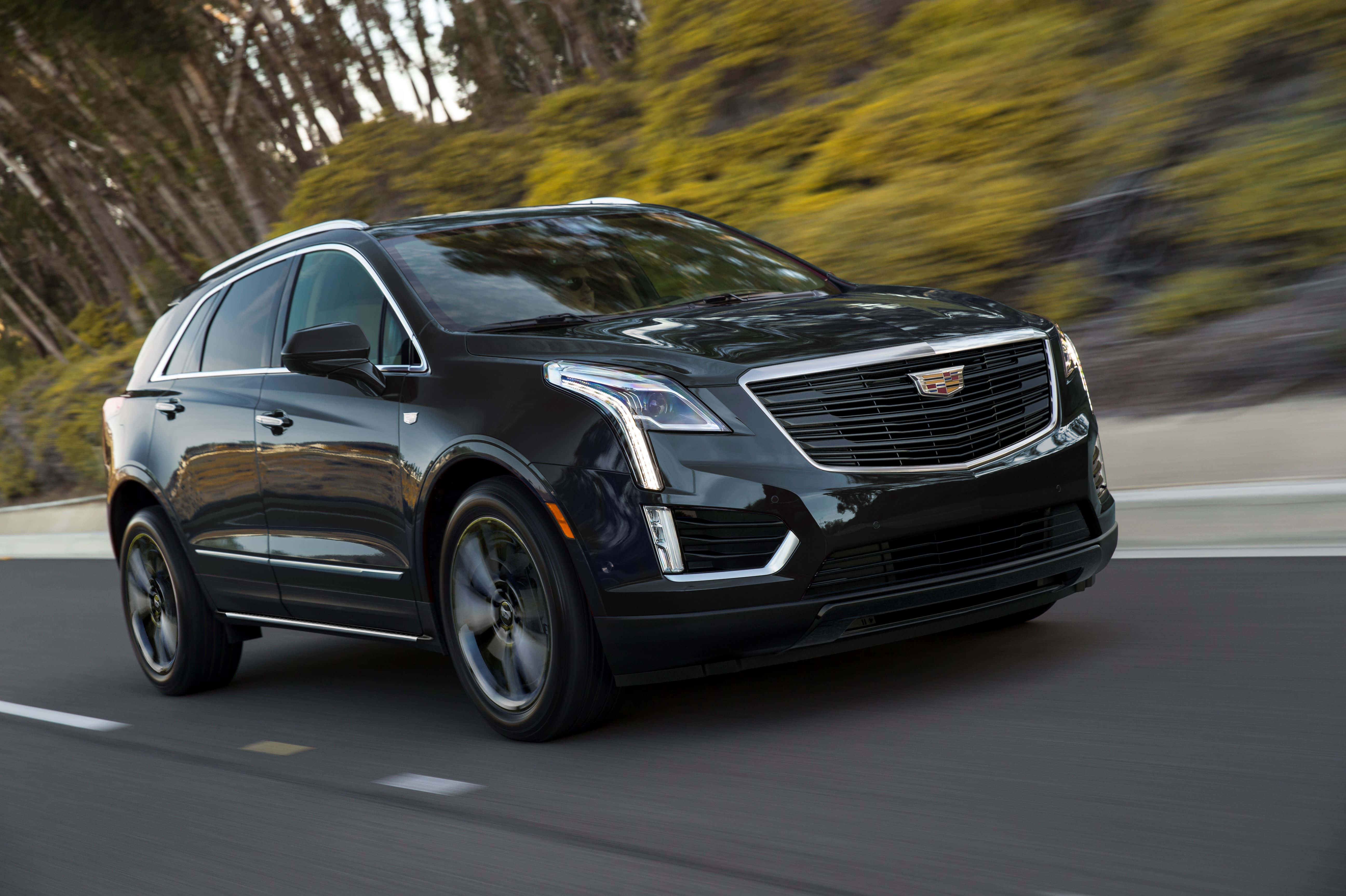 Cadillac Xt5 桌布 壁紙 — 一輛時尚的黑色凱迪拉克SUV沿著蜿蜒的道路穿過樹木繁茂的山坡，綠意模糊。