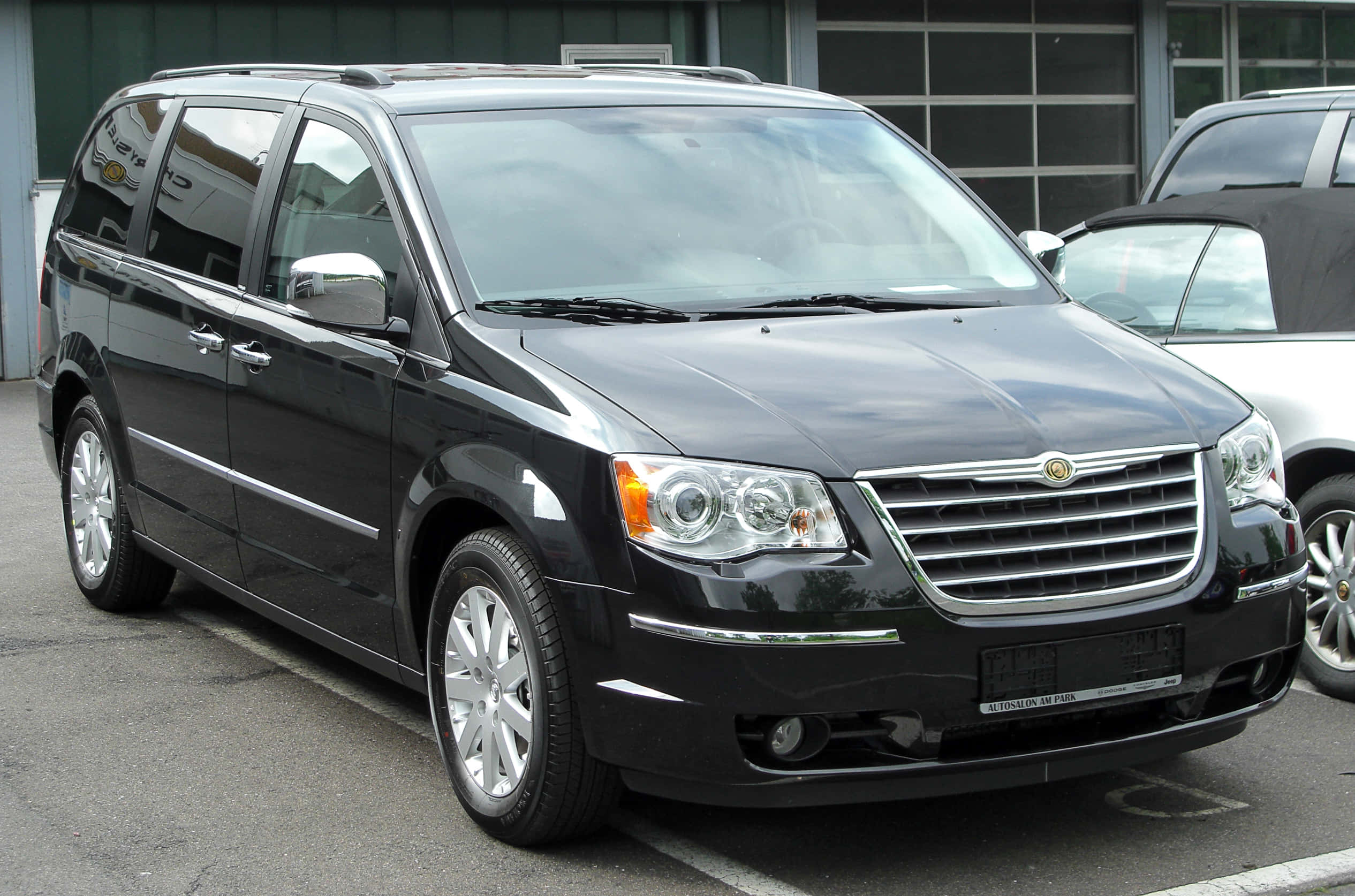 Chrysler Voyager 桌布 壁紙 — 一輛時尚的黑色克萊斯勒Town and Country廂型車停放在停車場，背景有現代建築。