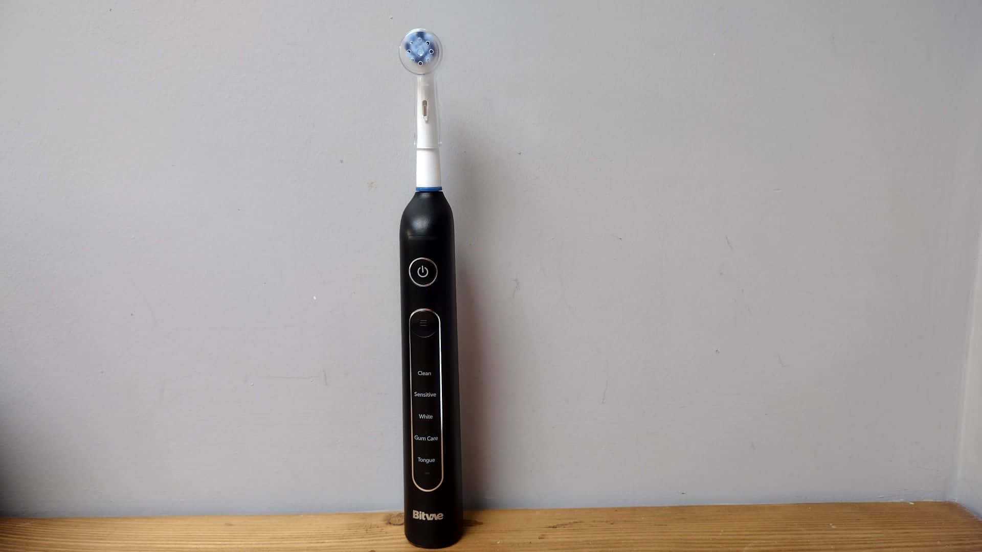  壁紙 — 一把時尚的黑色電動牙刷，帶有藍色刷毛頭，直立於木質表面上，背景為素色牆壁。