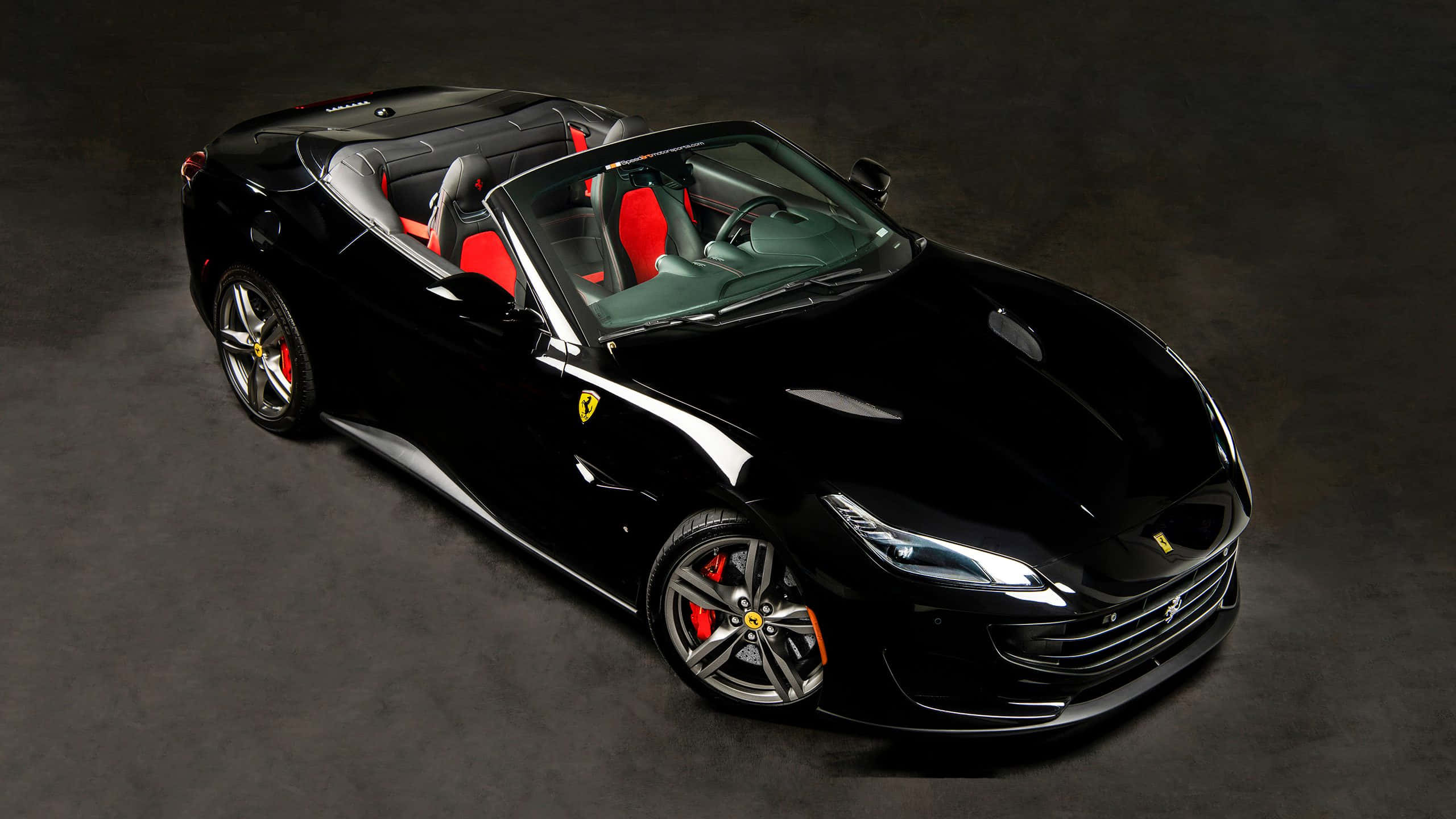 Ferrari Portofino 桌布 壁紙 — 一輛時尚的黑色法拉利敞篷車，配備紅色座椅和銀色輪圈，在深灰色背景下的攝影棚燈光中閃閃發光。