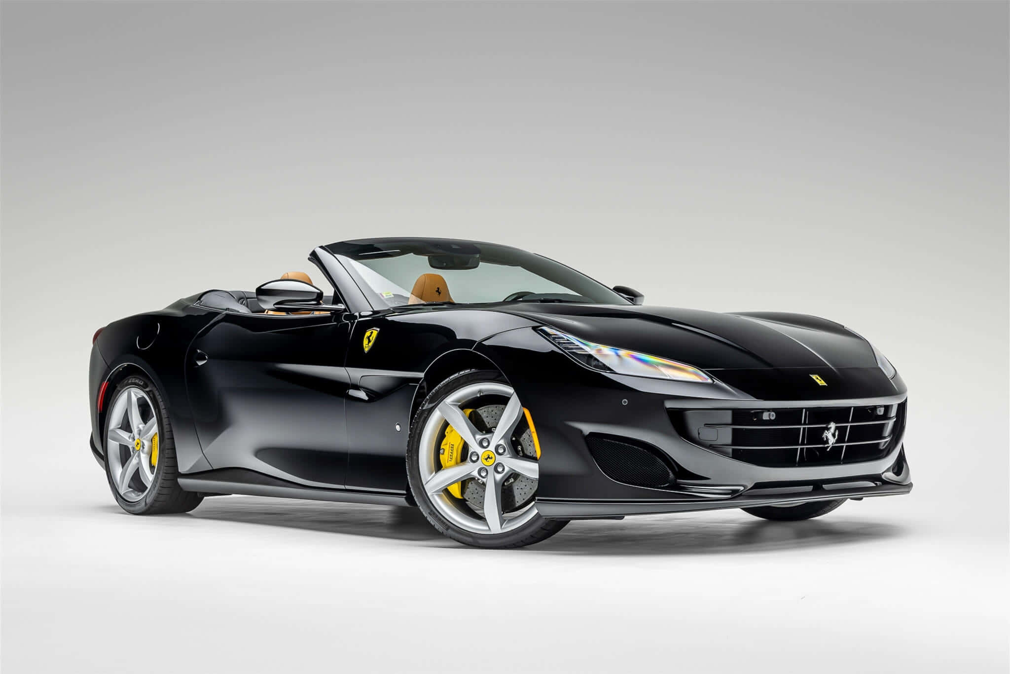 Ferrari Portofino 桌布 壁紙 — 一輛時尚的黑色法拉利敞篷車，帶有黃色制動卡鉗和米色內飾，擺放在極簡的白色工作室背景前。