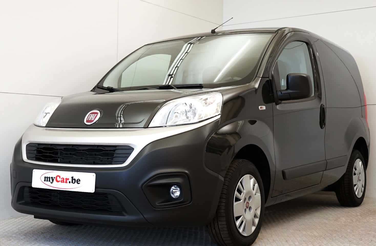 Fiat Fiorino 桌布 壁紙 — 一架時尚黑色Fiat廂型車帶有銀色飾邊，停放在室內灰色地板上，背景是純白色牆壁。
