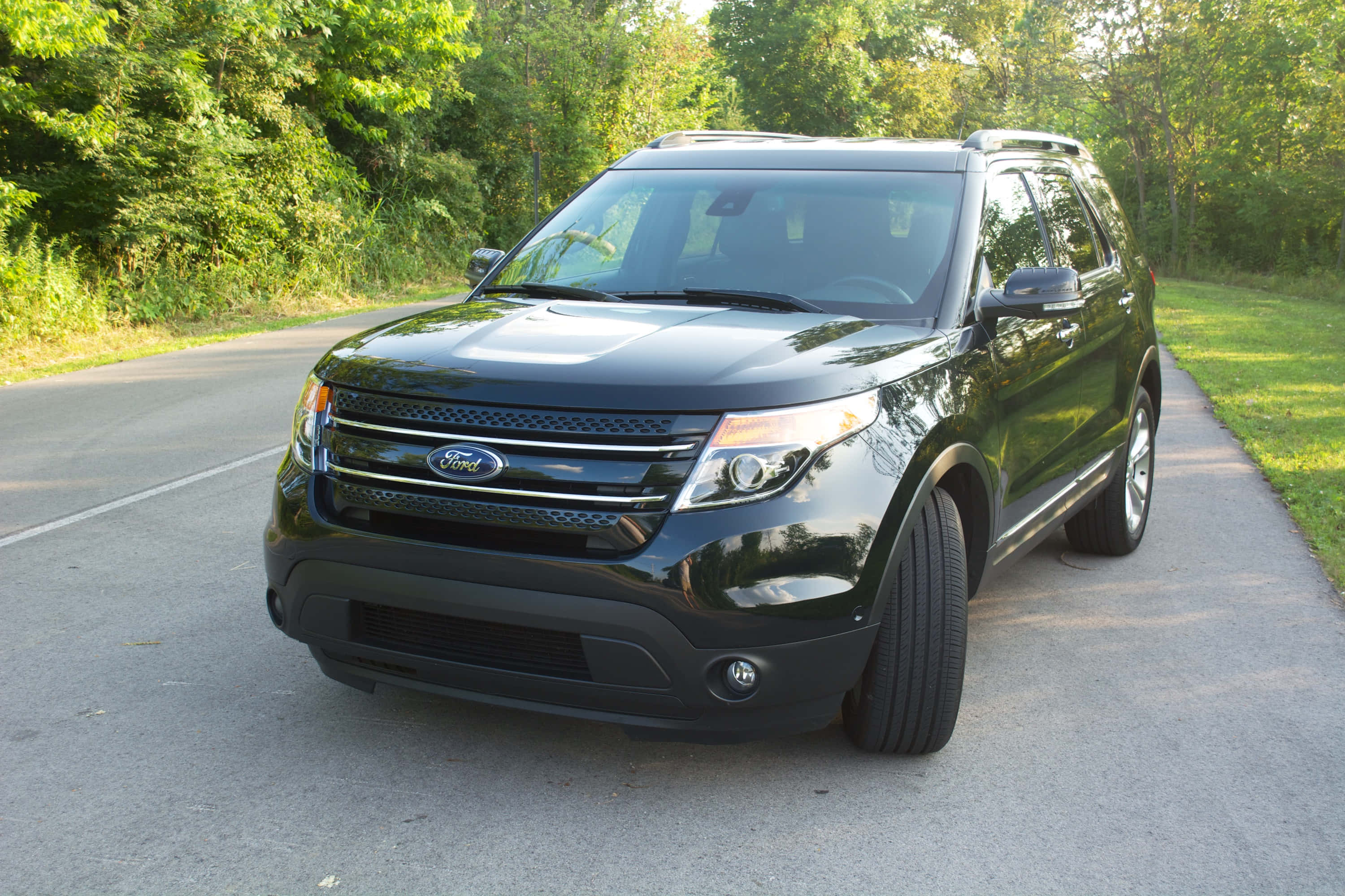 Ford Explorer 桌布 壁紙 — 一輛時尚的黑色福特Explorer SUV停泊在寧靜的柏油路上，兩旁綠樹成蔭，草地茂盛。