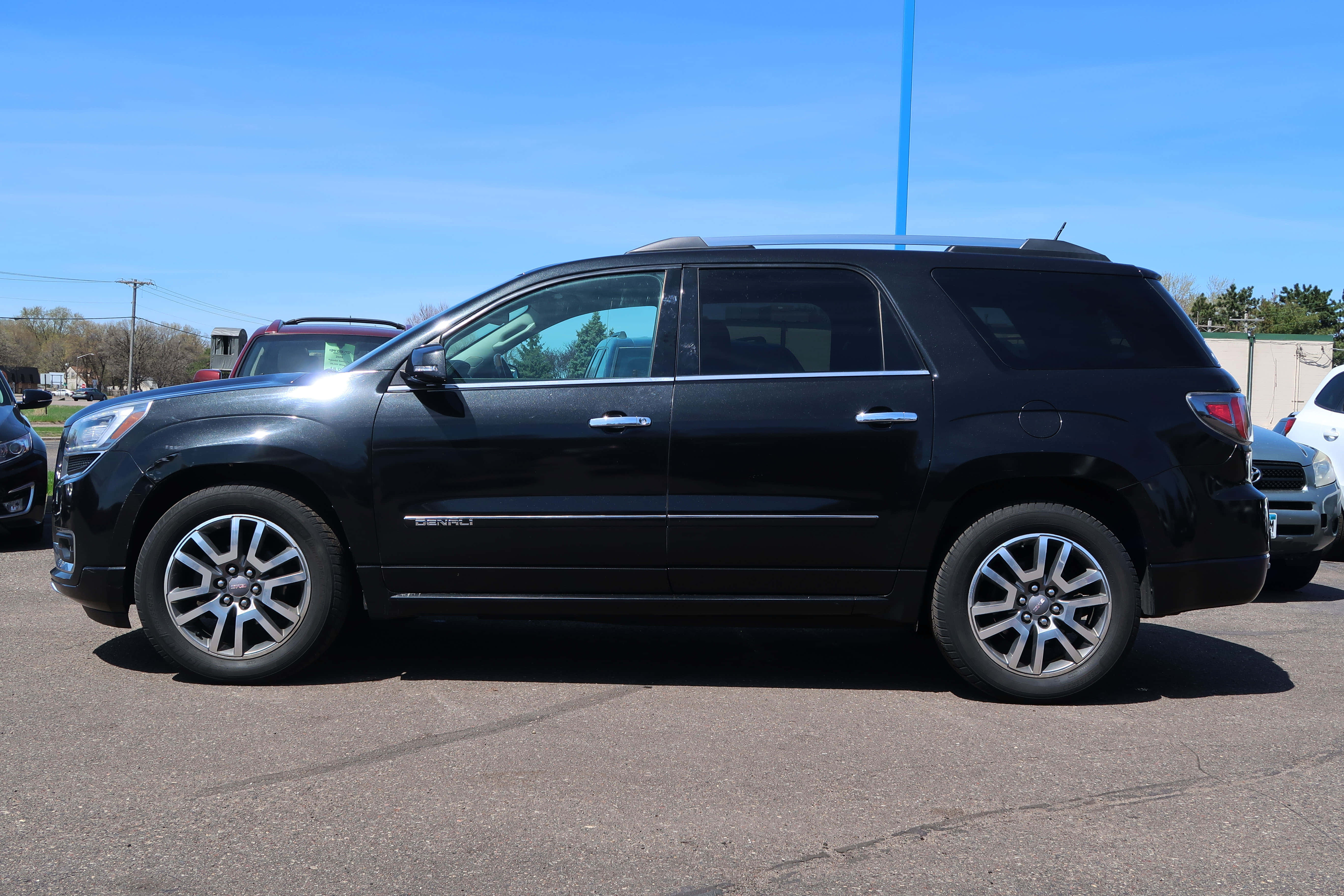 Gmc Acadia 桌布 壁紙 — 一輛時尚的黑色GMC Acadia SUV停放在陽光明媚的停車場，天空清澈湛藍，附近有其他車輛。