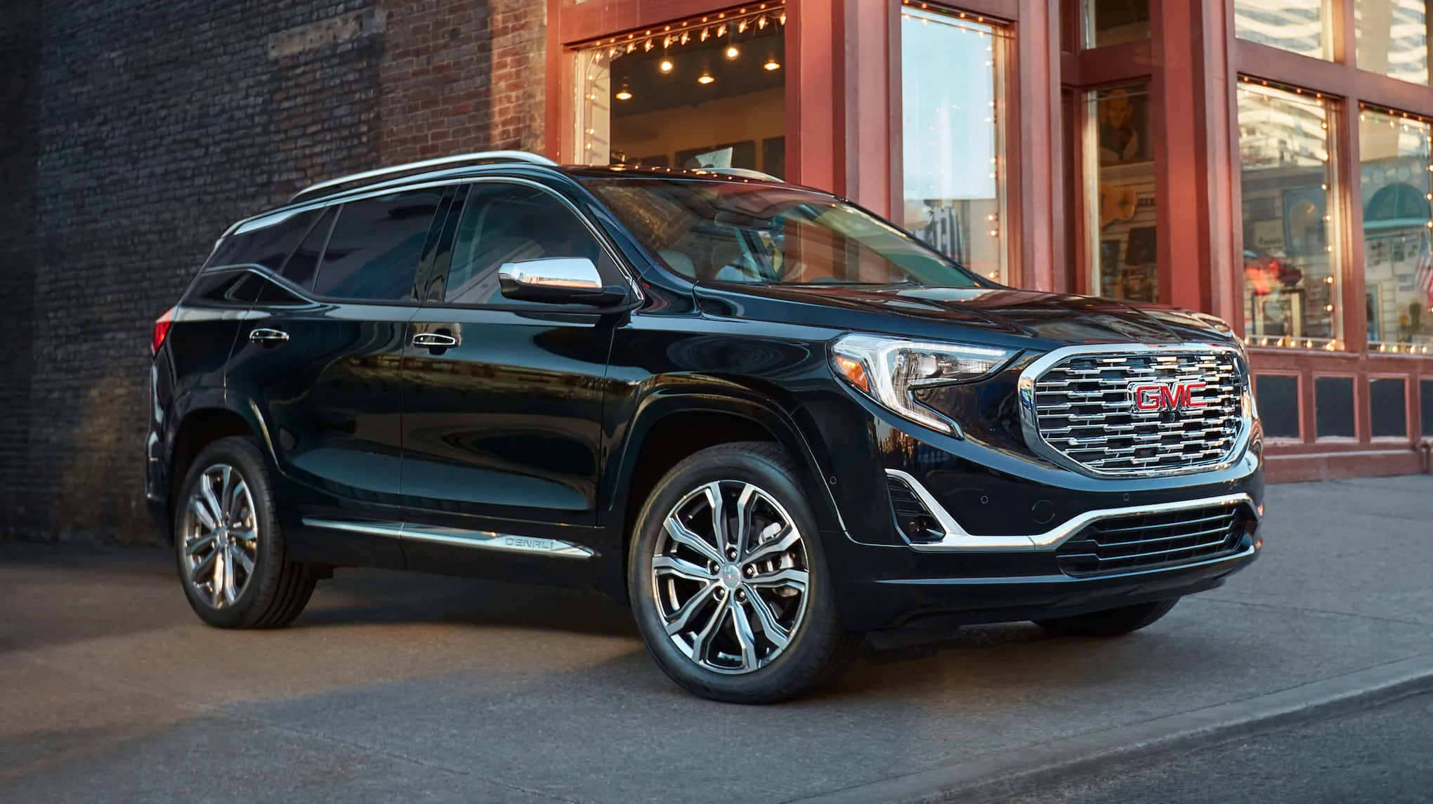 Gmc Terrain 桌布 壁紙 — 一輛時尚的黑色GMC Acadia SUV停放在城市街道上，旁邊是一棟帶有溫暖窗燈的磚造建築。
