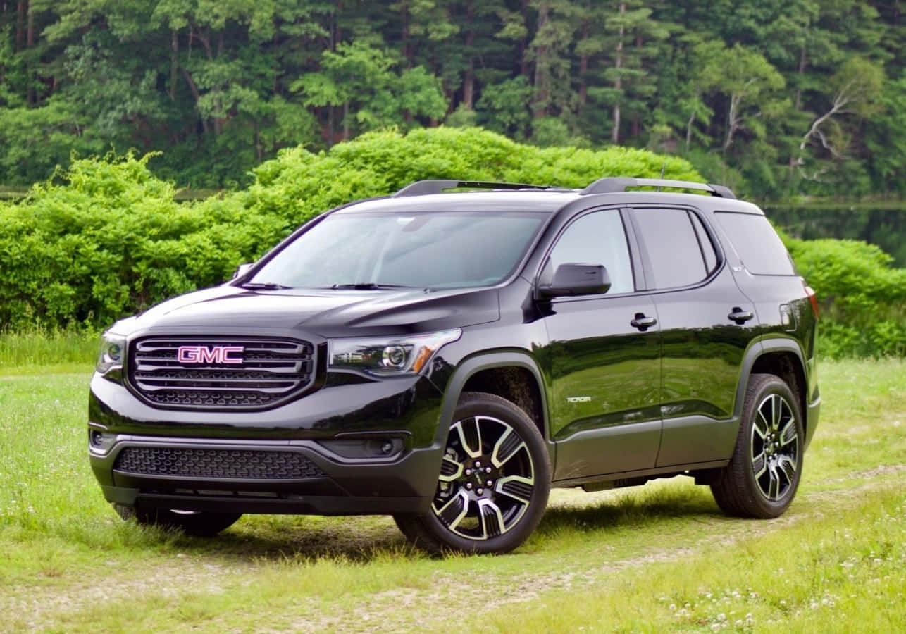 Gmc Acadia 桌布 壁紙 — 一輛時尚的黑色GMC Acadia SUV停在草地上，背景是茂密的綠色樹木和灌木叢。