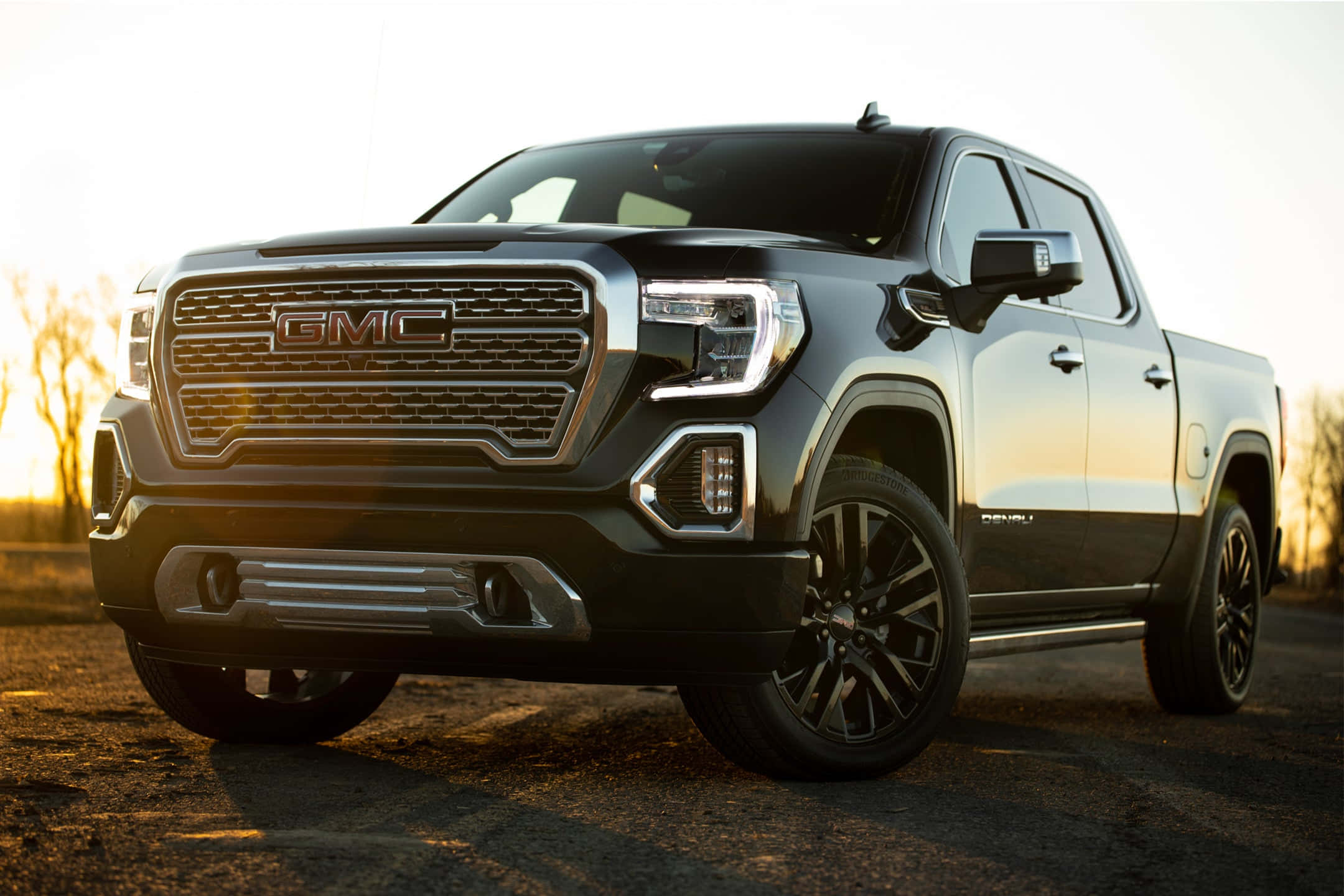 Gmc Sierra 桌布 壁紙 — 一輛時尚的黑色GMC Sierra Denali皮卡車在碎石路上閃耀著金色的夕陽光輝。
