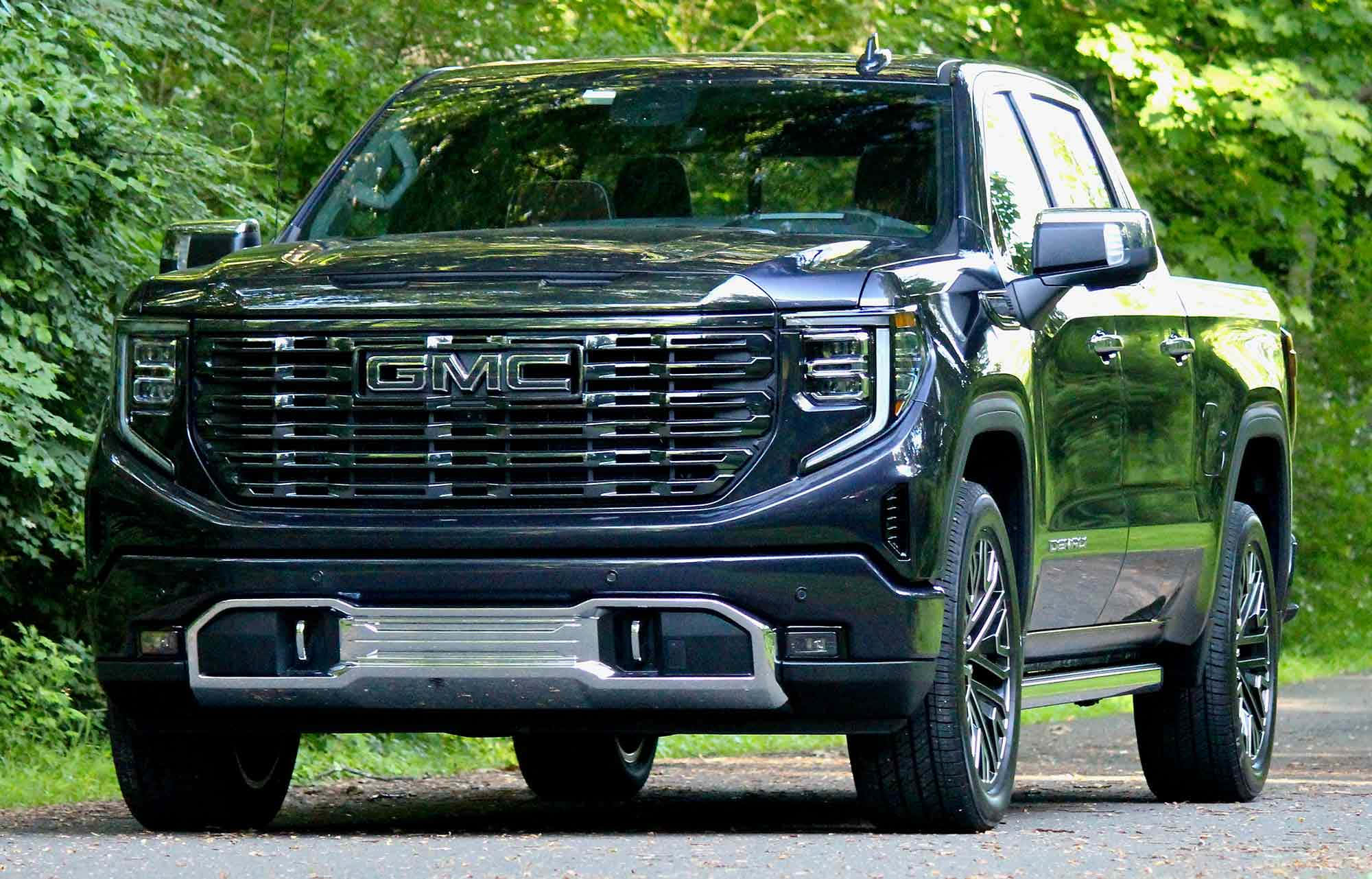 Gmc Sierra 桌布 壁紙 — 一輛時尚的黑色GMC Sierra Denali皮卡車停在碎石路上，周圍是茂密的綠色森林。