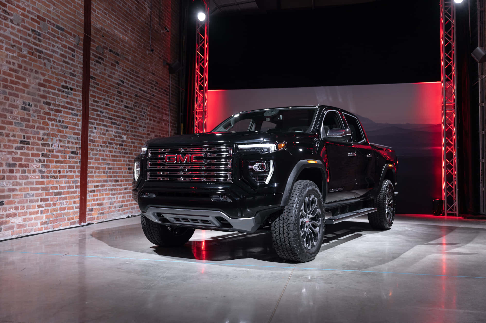 Gmc Canyon 桌布 壁紙 — 一輛時尚的黑色GMC Sierra卡車在戲劇性的紅色燈光下，以磚牆和黑暗背景展示。