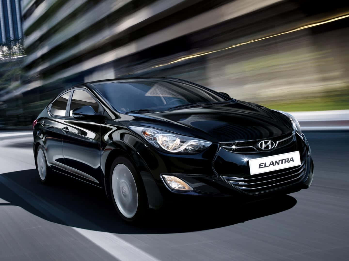 Hyundai Elantra 桌布 壁紙 — 一輛時尚的黑色現代Elantra在模糊的城市街道上疾馳，動態模糊強調了速度。