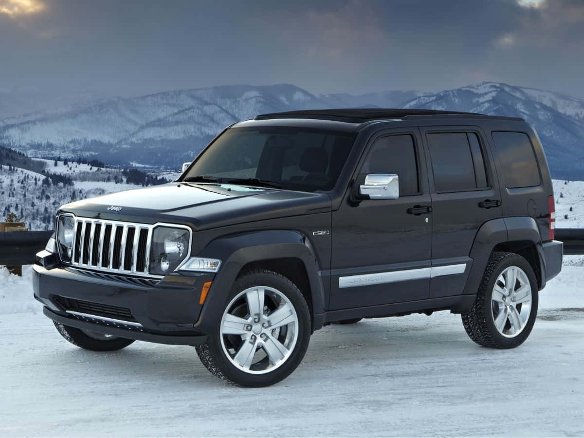 Jeep Liberty 桌布 壁紙 — 一輛時尚的黑色Jeep Liberty停在積雪的路邊，白雪覆蓋的山脈在陰沉的暮色天空下若隱若現。