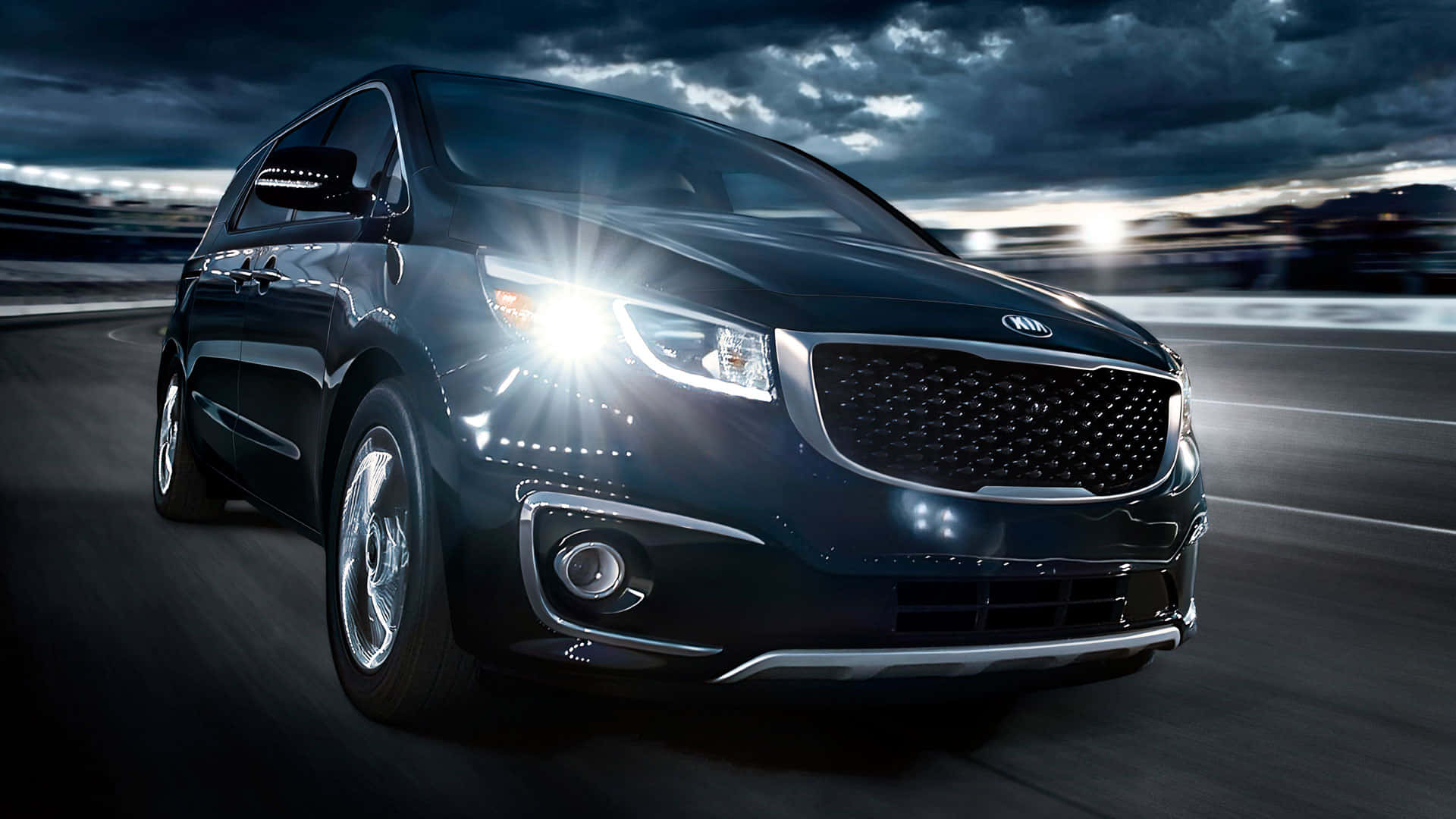 Kia Sedona 桌布 壁紙 — 一輛時尚的黑色起亞SUV在潮濕的道路上疾馳，發光的車頭燈劃破暴風雨黃昏的天空。