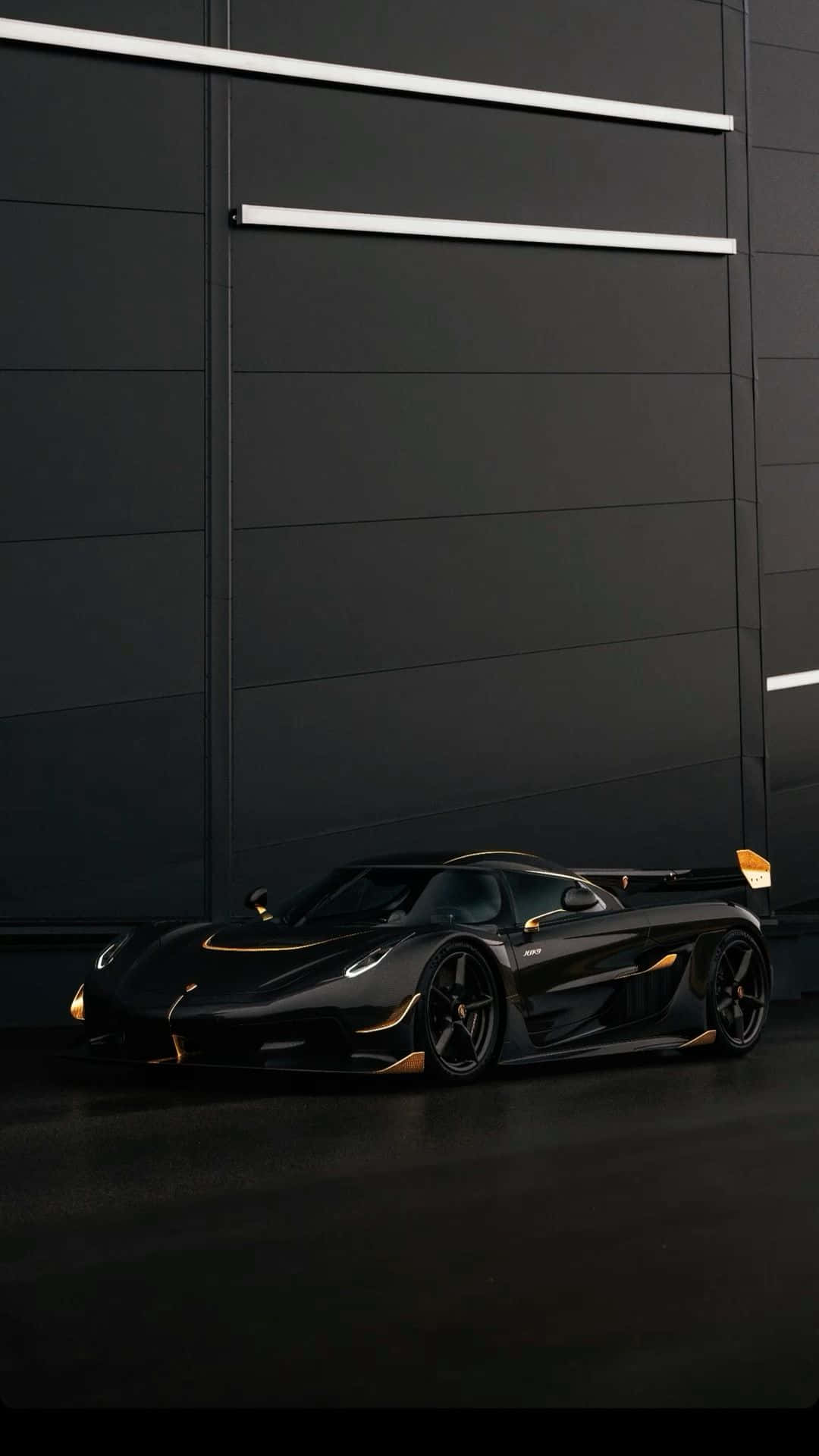  壁紙 — 一輛時尚的黑色Koenigsegg超級跑車，帶有金色點綴，停在簡約的深色工業牆前。