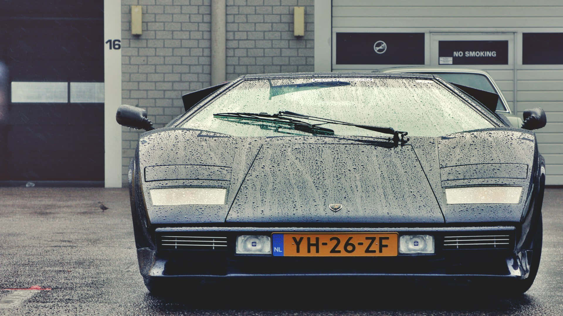 Lamborghini Countach 桌布 壁紙 — 一輛流線型黑色藍寶堅尼Countach停在車庫前，雨滴在其標誌性的棱角車身上閃閃發光。