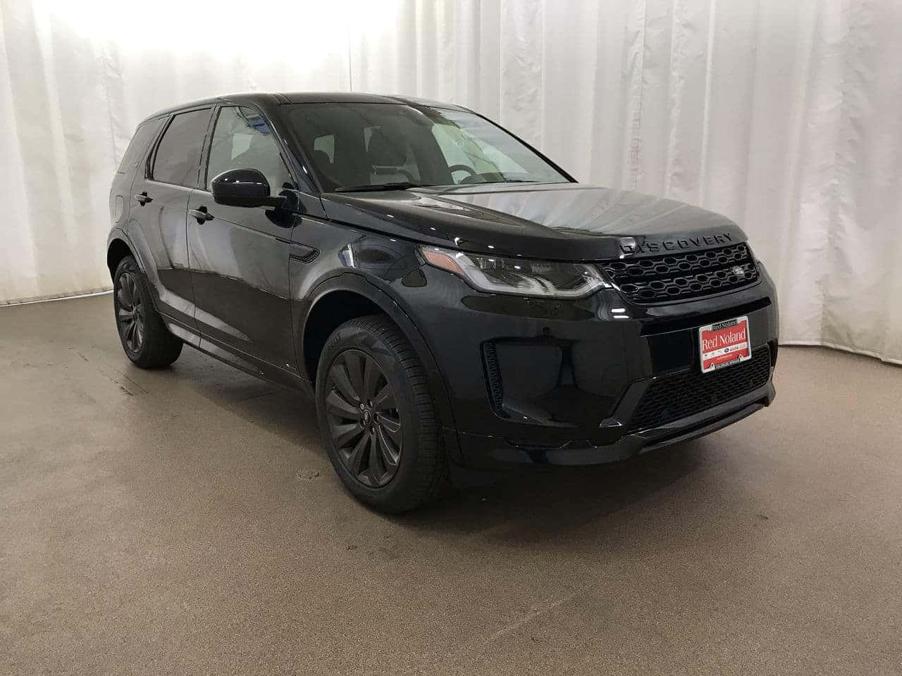 Land Rover Discovery 桌布 壁紙 — 一輛時尚的黑色 Land Rover Discovery SUV 在室內以白色窗簾背景和經銷商車牌展示。