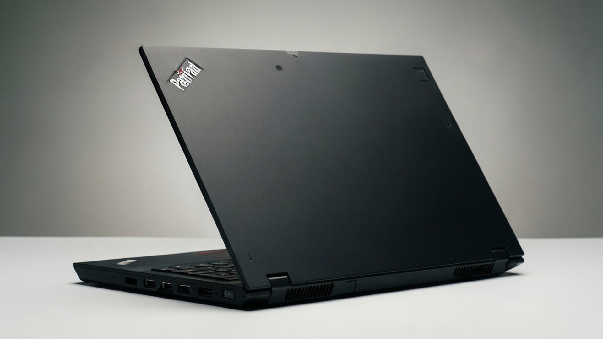 Thinkpad 桌布 壁紙 — 一部時尚的黑色 Lenovo ThinkPad 筆記型電腦在白色表面上打開，背景為柔和的灰色。