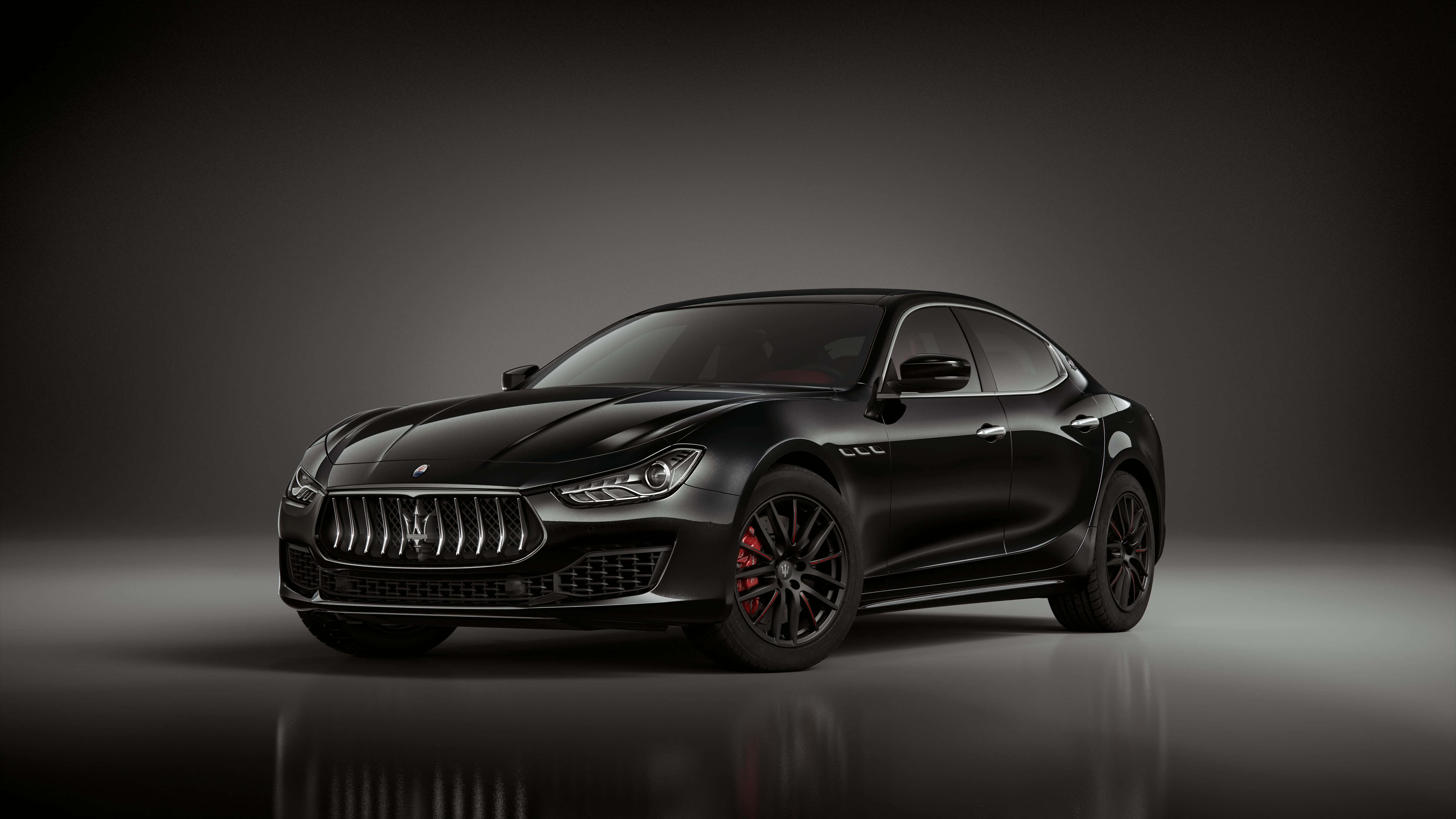 Maserati Ghibli 桌布 壁紙 — 一輛時尚的黑色瑪莎拉蒂跑車配備紅色制動卡鉗，在攝影棚燈光下於反光地板上閃耀。
