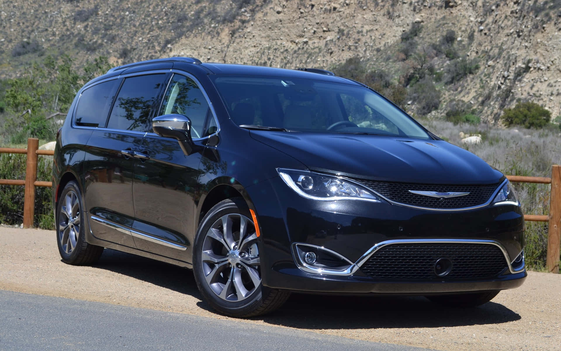 Chrysler Pacifica 桌布 壁紙 — 一輛時尚黑色小型貨車停泊在碎石路上，旁邊有木柵欄，背景是岩石丘陵。