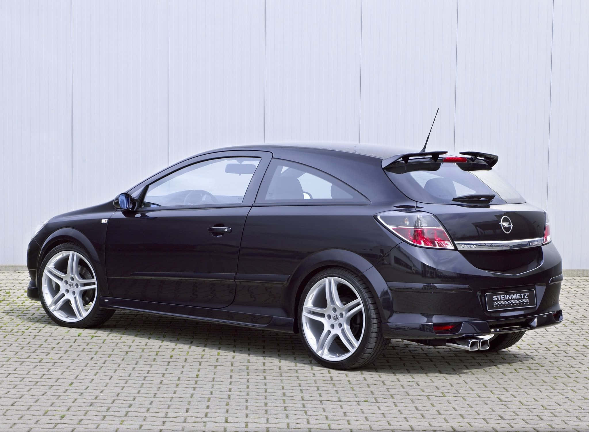 Opel Astra 桌布 壁紙 — 一輛時尚黑色改裝Opel Astra GTC跑車，停放在鋪砌路面上，背景為淺灰色牆壁。
