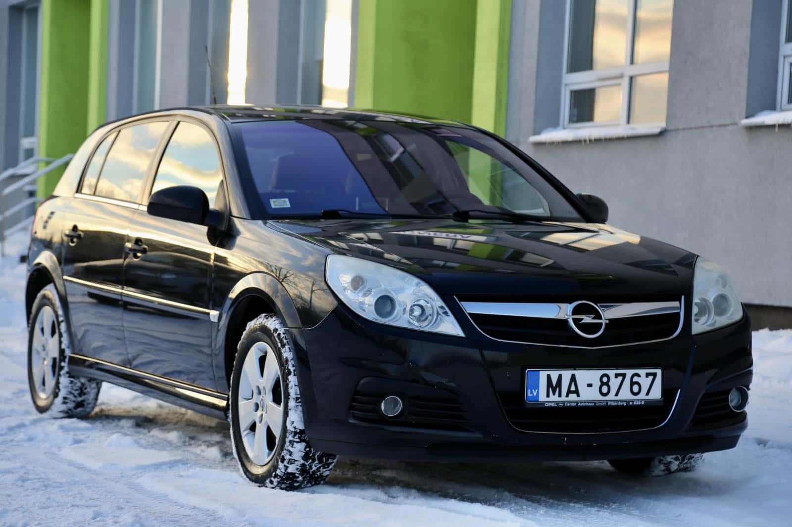  壁紙 — 一輛時尚的黑色Opel Astra停放在雪地上，背景是一座現代建築。