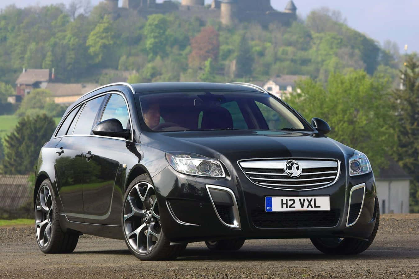 Opel Insignia 桌布 壁紙 — 一輛時尚的黑色歐寶Insignia Sports Tourer停泊在碎石上，背景有城堡和綠色山丘。