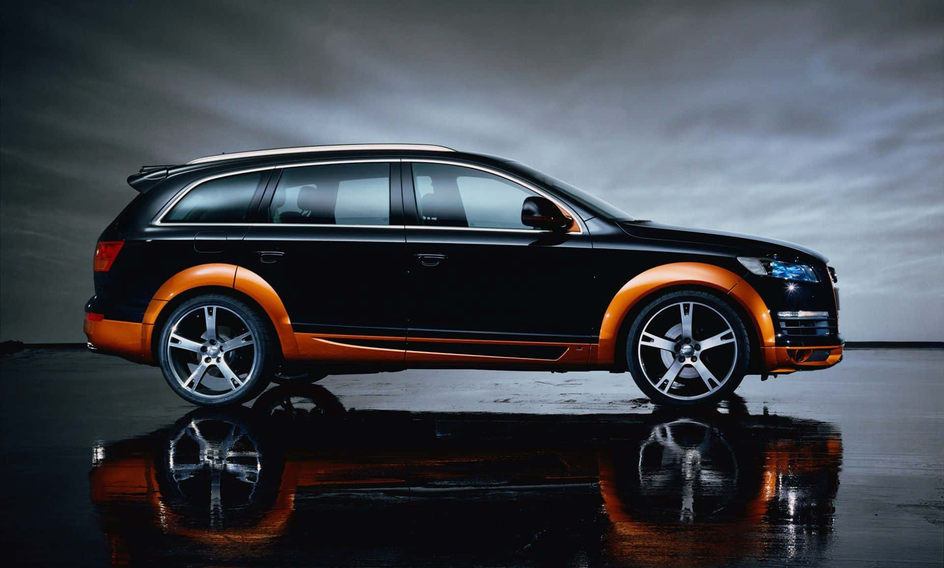 Audi Q7 桌布 壁紙 — 一輛時尚的黑色和橙色SUV在陰沉多雲的天空下，停在潮濕的反光表面上。