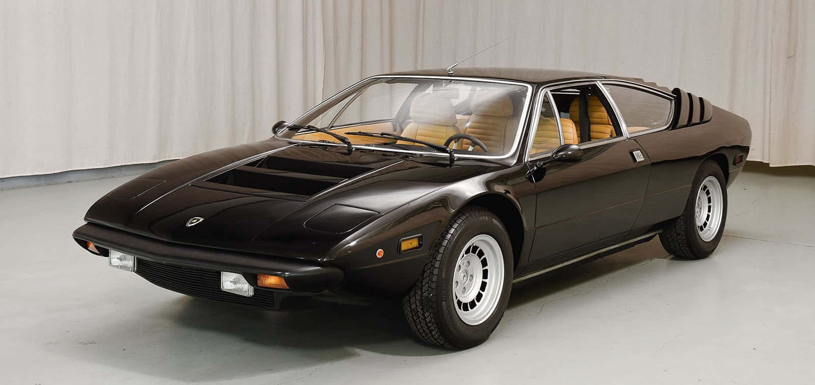 Lamborghini Urraco 桌布 壁紙 — 一輛時尚的黑色復古跑車，配以米色內裝，在簡約的攝影棚環境中展示。