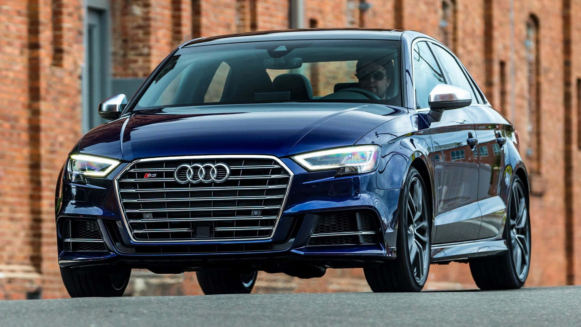 Audi S3 桌布 壁紙 — 一輛時尚的藍色奧迪RS3轎車在日光下閃閃發光，停在風化的磚砌建築前。
