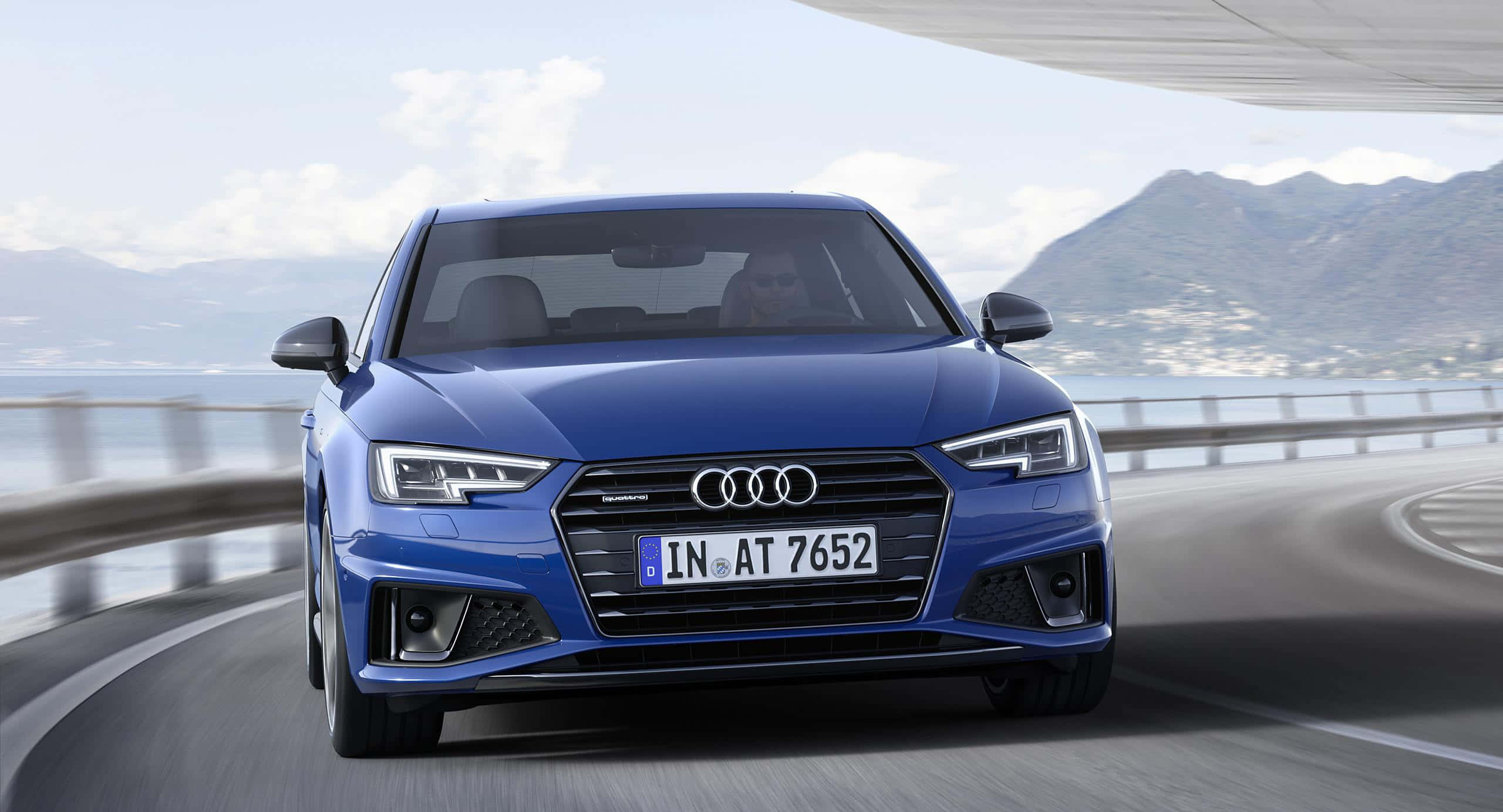 Audi A4 桌布 壁紙 — 一輛時尚的藍色奧迪轎車沿著海岸公路飛馳，背景是山脈和海洋。