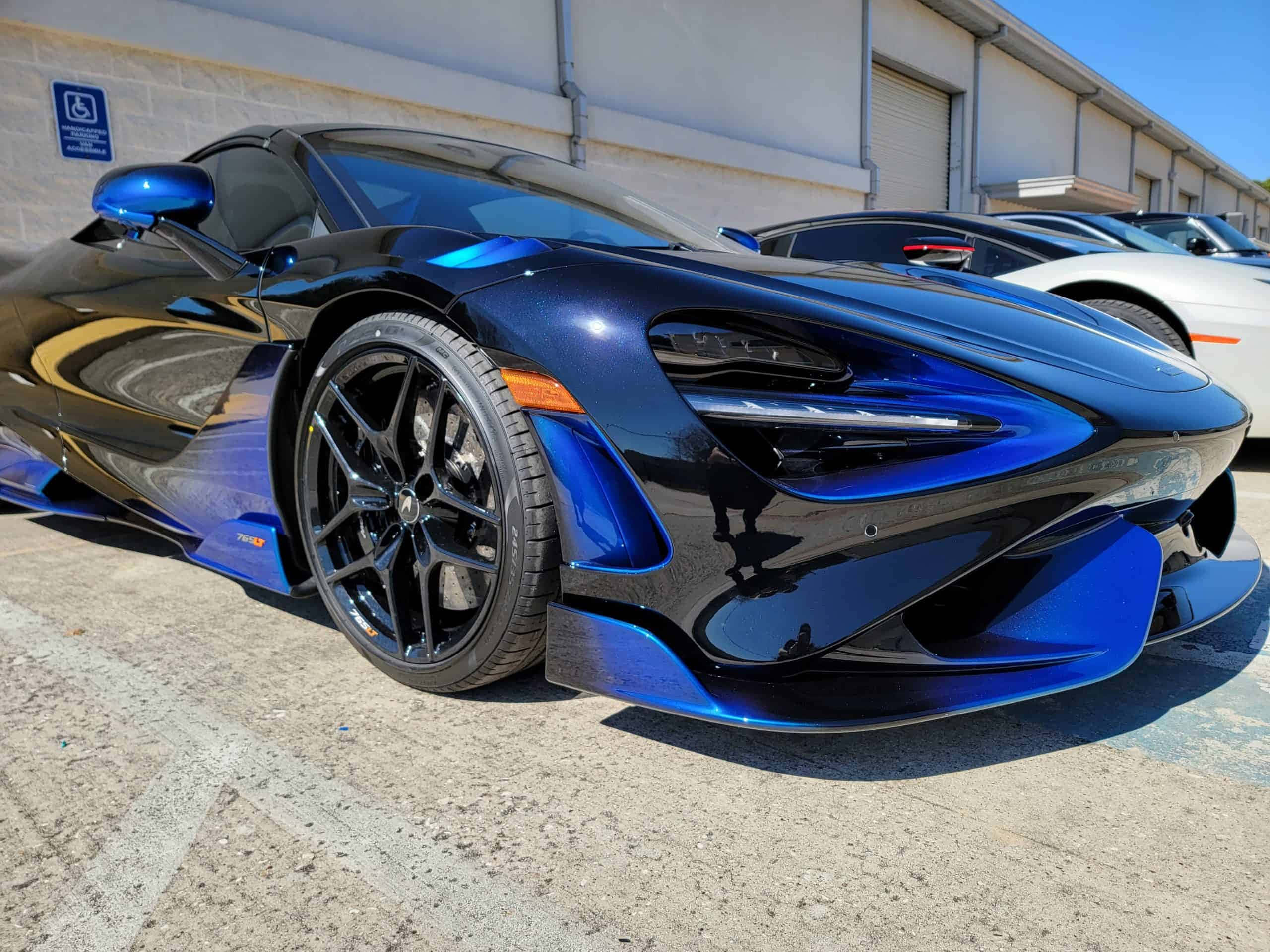 Mclaren 765lt 桌布 壁紙 — 一架時尚的藍黑McLaren跑車在明亮的陽光下閃閃發光，停放在工業區。