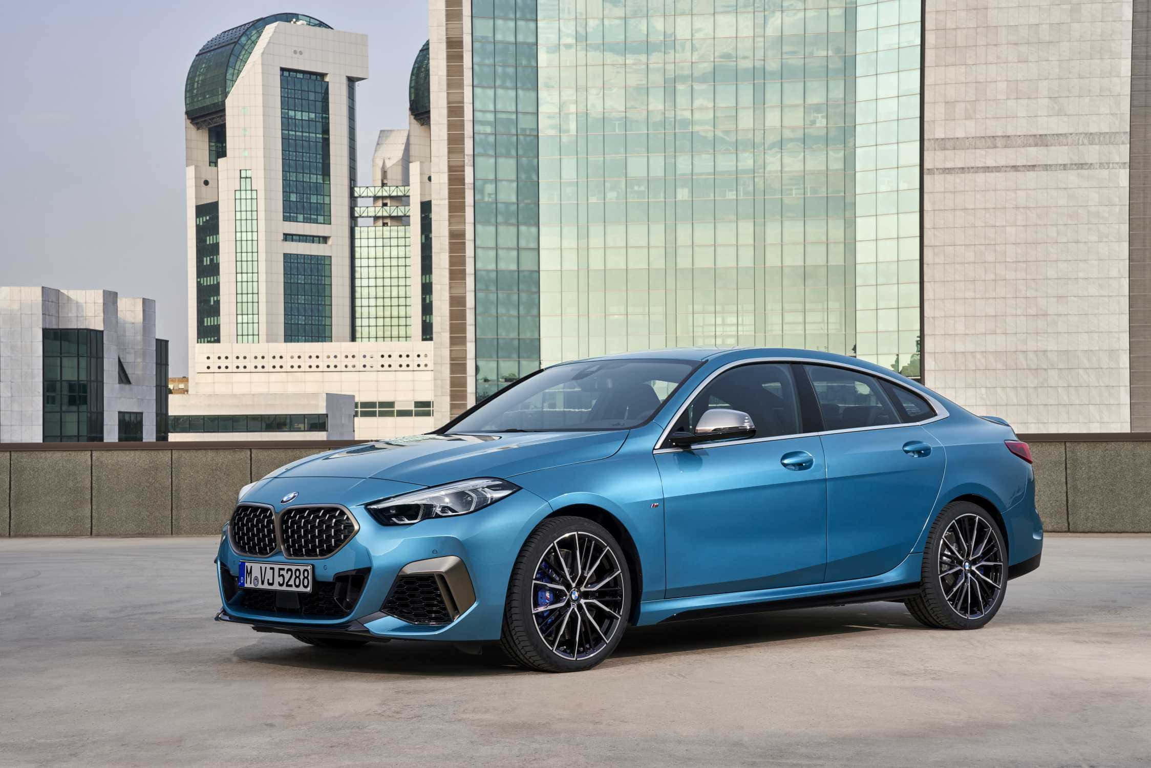 Bmw 2 Series 桌布 壁紙 — 一輛時尚的藍色寶馬轎車停放在屋頂上，現代玻璃摩天大樓在其閃亮表面反射。