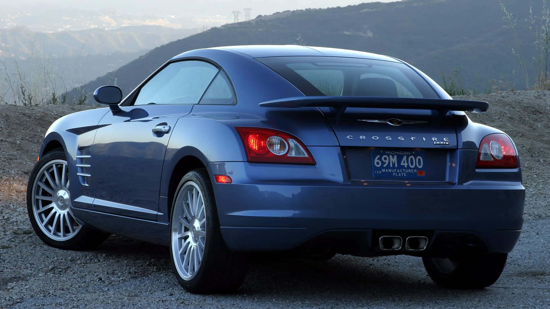 Chrysler Crossfire 桌布 壁紙 — 一輛流線型藍色 Chrysler Crossfire 跑車停泊在碎石山坡上，背景有山巒。
