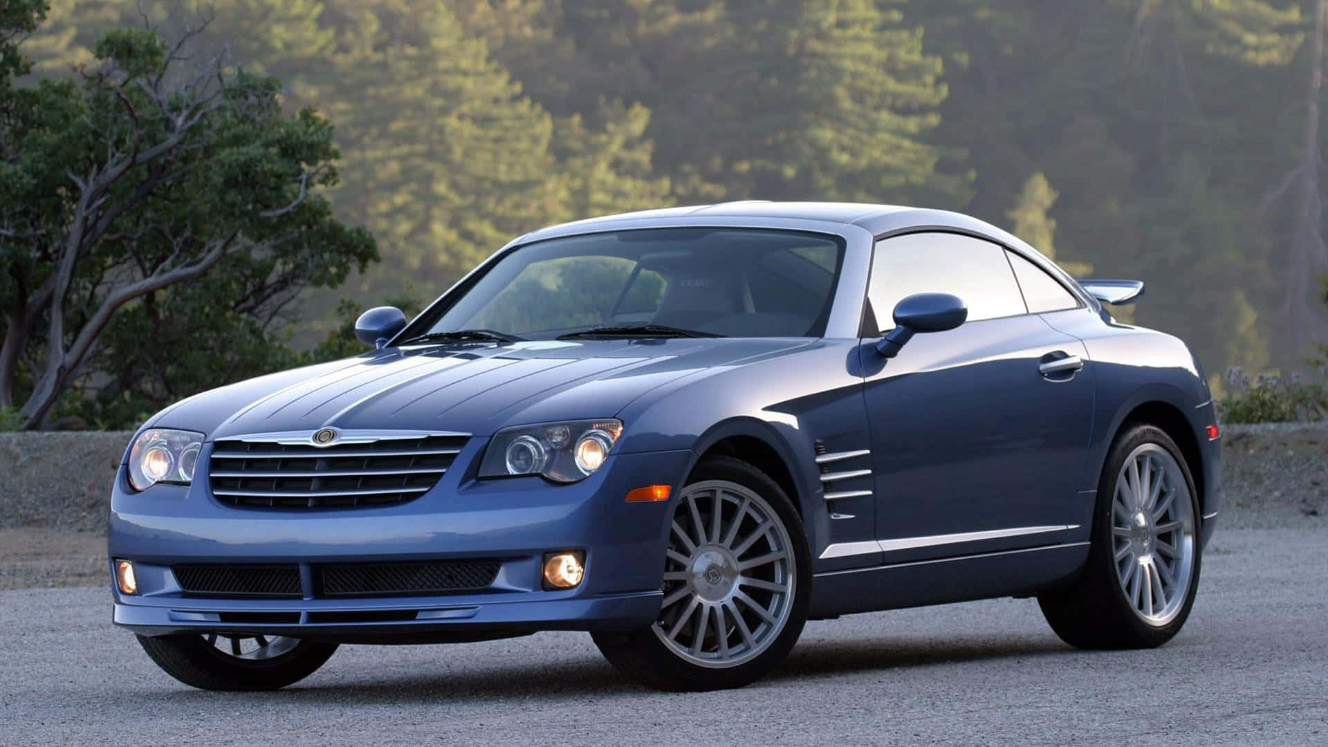 Chrysler Crossfire 桌布 壁紙 — 一輛時尚的藍色 Chrysler Crossfire 跑車停在碎石路上，背景有樹木和山丘。