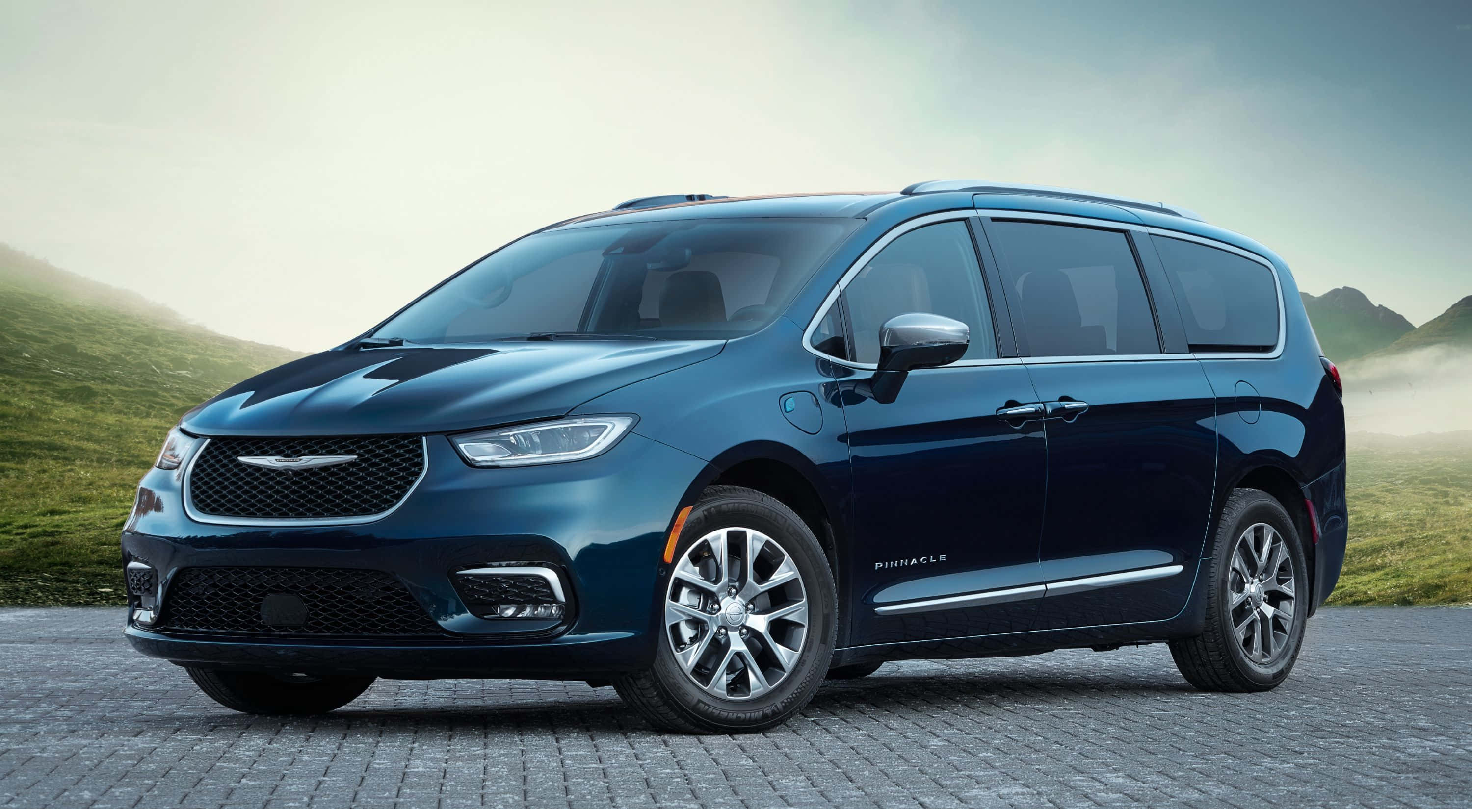 Chrysler Pacifica 桌布 壁紙 — 一輛時尚的藍色 Chrysler Pacifica 小型貨車停泊在鵝卵石路上，背景是霧氣瀰漫的綠色山丘。