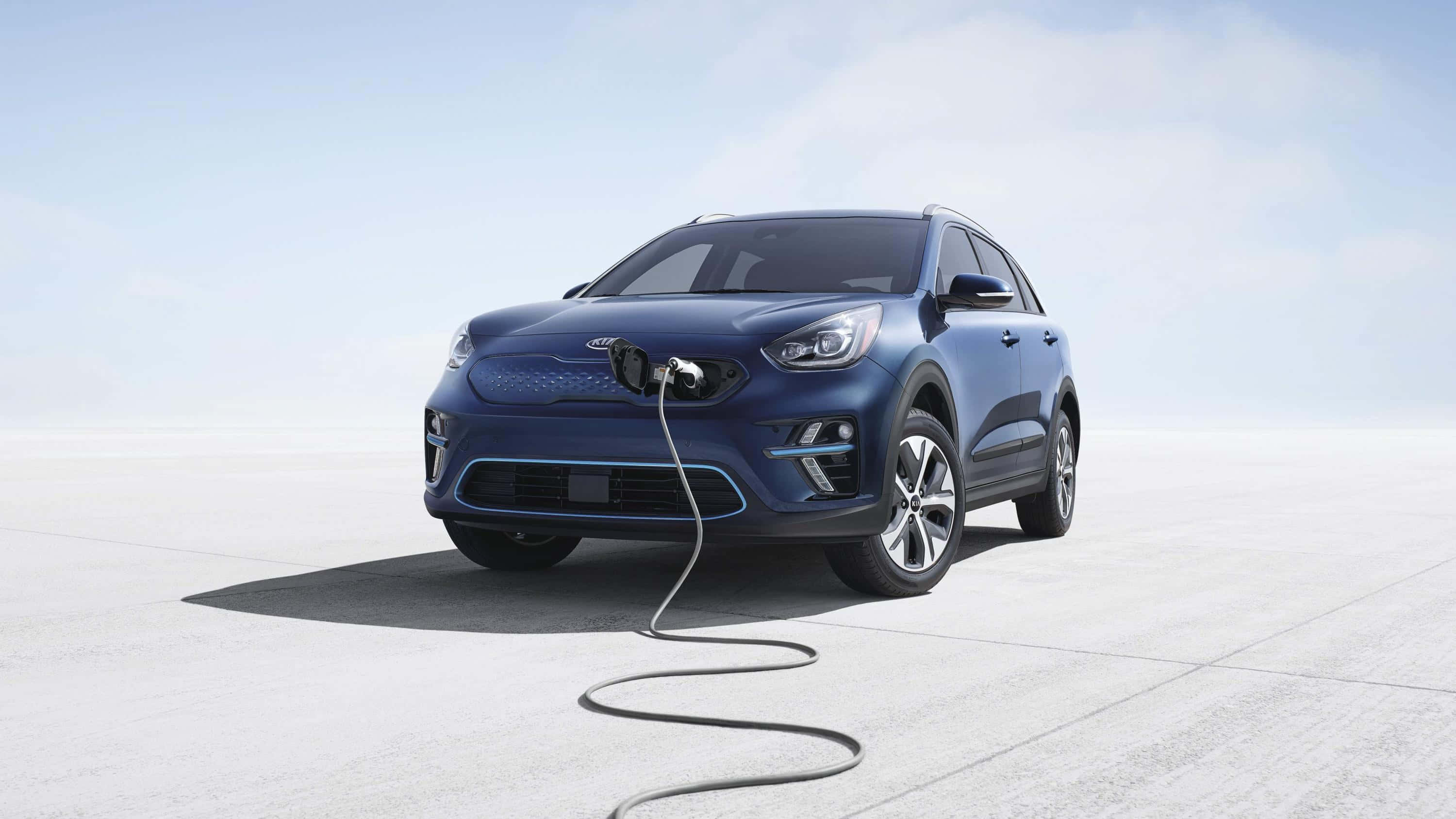 Kia Niro 桌布 壁紙 — 一輛時尚的藍色電動SUV在晴朗天空下的簡約混凝土平台上充電。