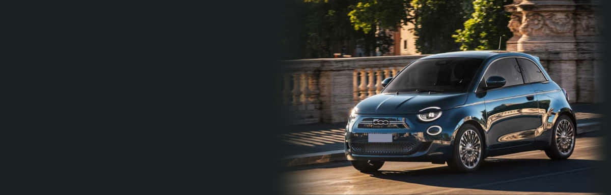 Fiat Tipo 桌布 壁紙 — 一輛時尚的藍色Fiat 500e電動車在金色陽光下閃耀，位於石造建築的綠樹成蔭城市街道上。