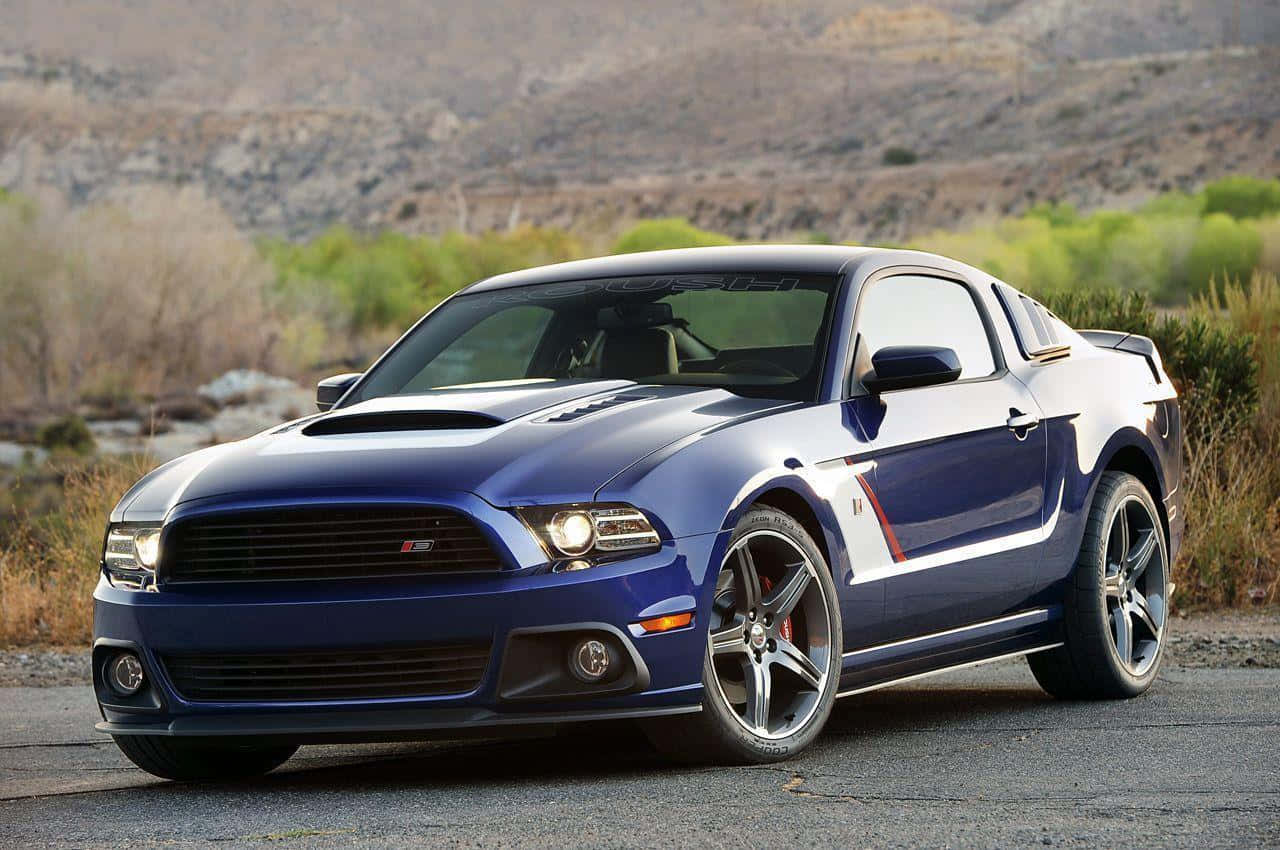 Ford Mustang Roush 桌布 壁紙 — 一輛時尚的藍色福特野馬Shelby GT500停泊在碎石路上，背景是乾旱的山丘和綠色灌木。