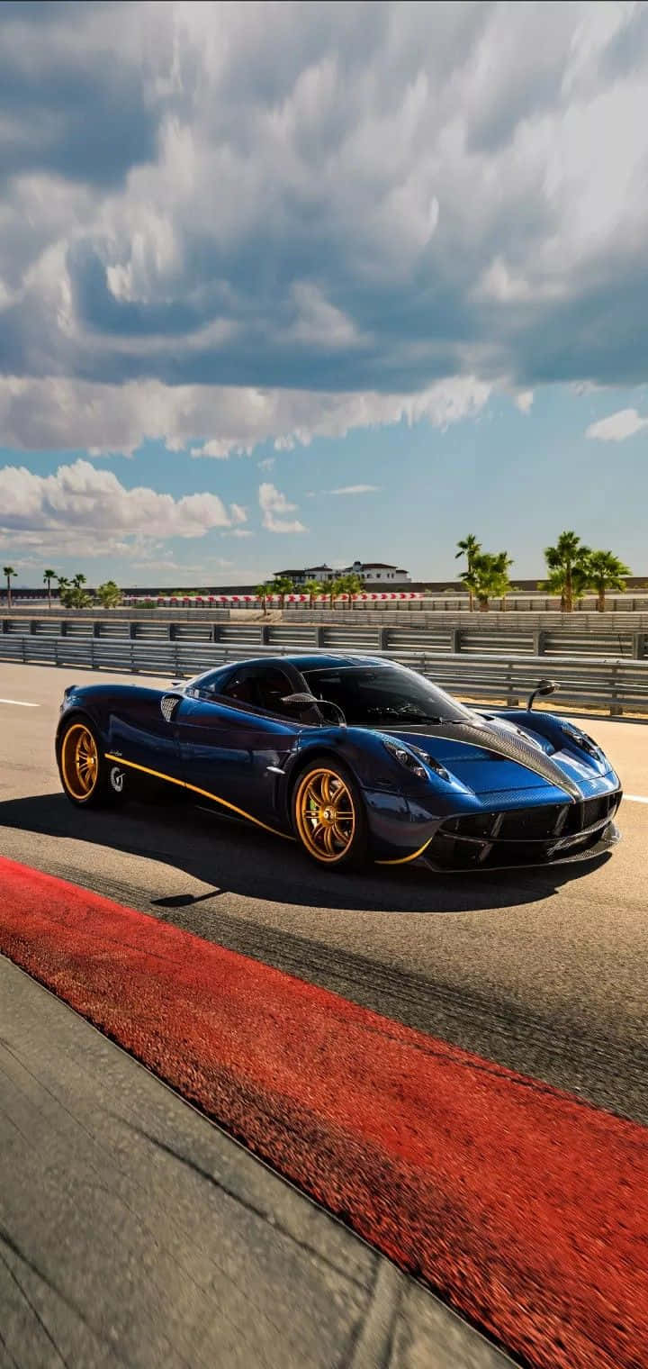 Pagani Huayra Roadster Bc 桌布 壁紙 — 一輛時尚的藍色超級跑車帶有金色點綴，在戲劇性的多雲天空下沿著賽道飛馳。