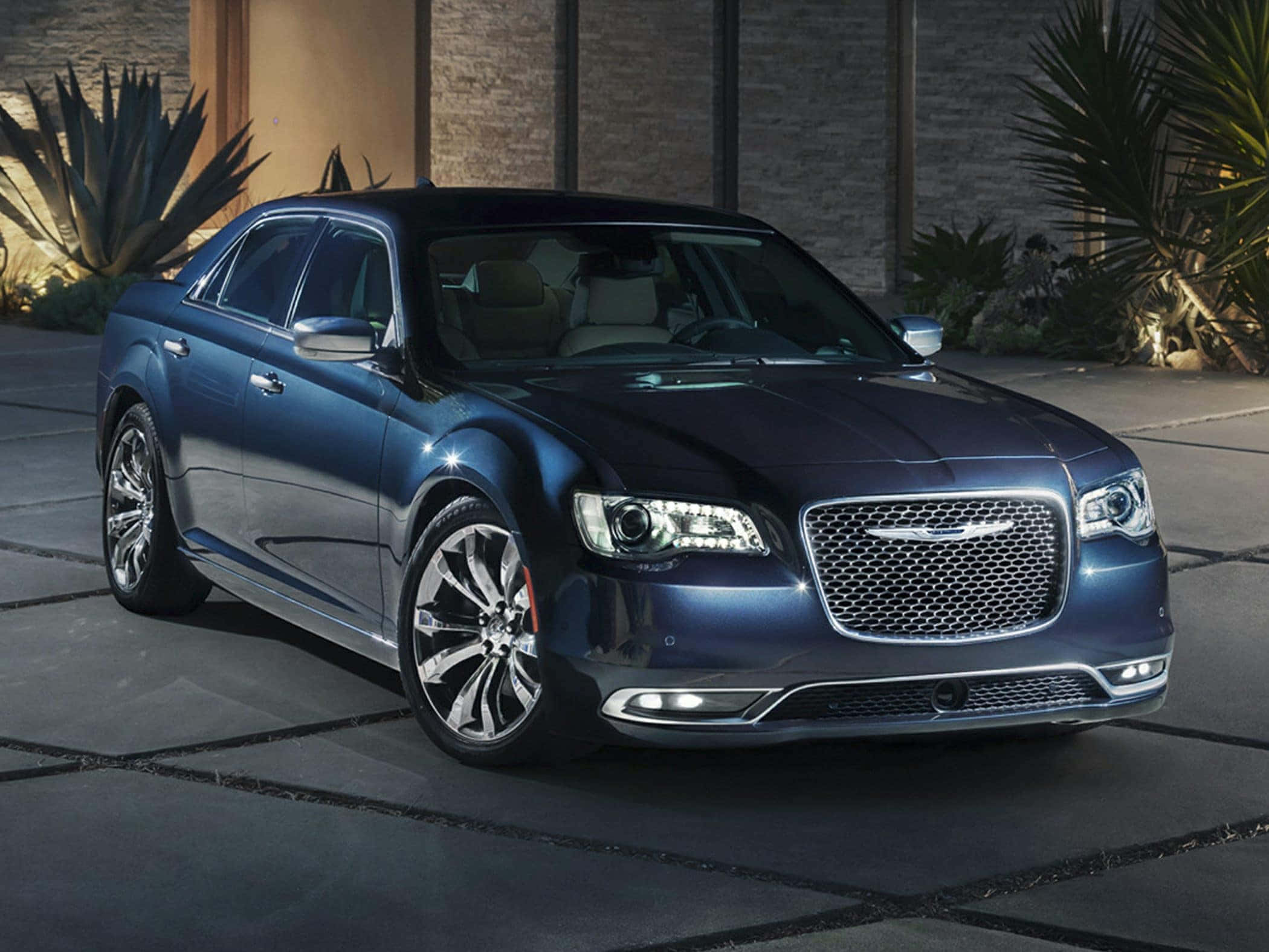 Chrysler 300 桌布 壁紙 — 一輛時尚的藍色豪華轎車在晚間燈光下閃閃發光，停在石頭車道上，旁邊是沙漠植物。