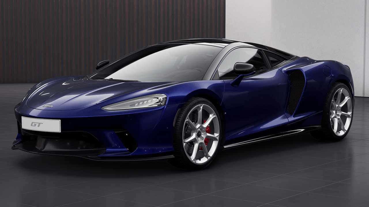 Mclaren Gt 桌布 壁紙 — 一輛時尚的藍色McLaren GT跑車在攝影棚燈光下閃閃發光，背景為深色木材和白色牆壁。