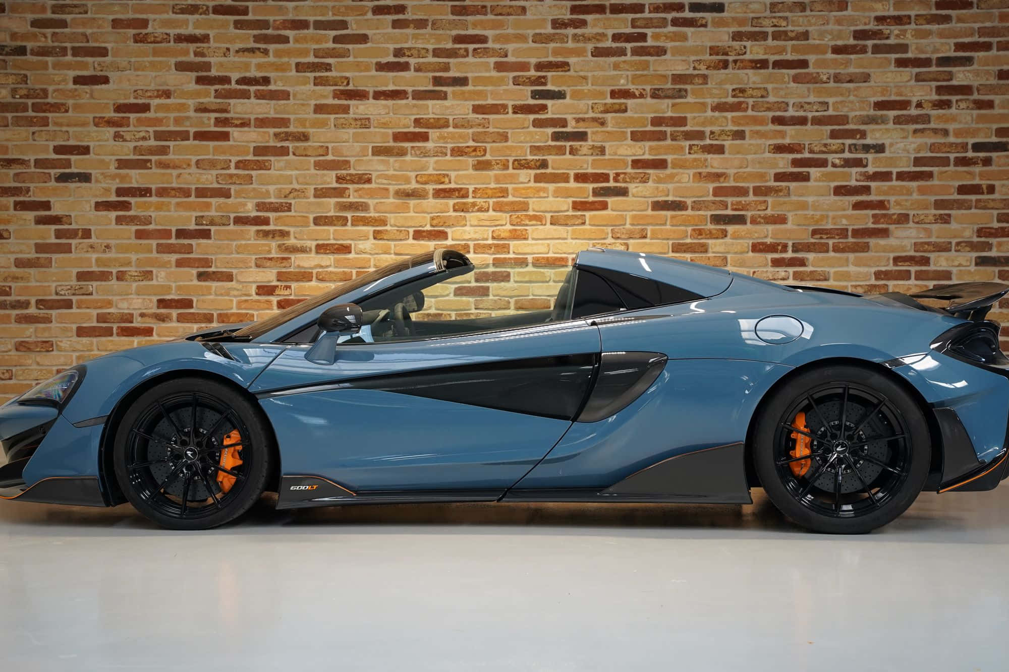 Mclaren 600lt Spider 桌布 壁紙 — 一輛時尚的藍色McLaren Speedtail敞篷跑車，帶有橙色制動卡鉗，側面靠在溫暖的磚牆上。