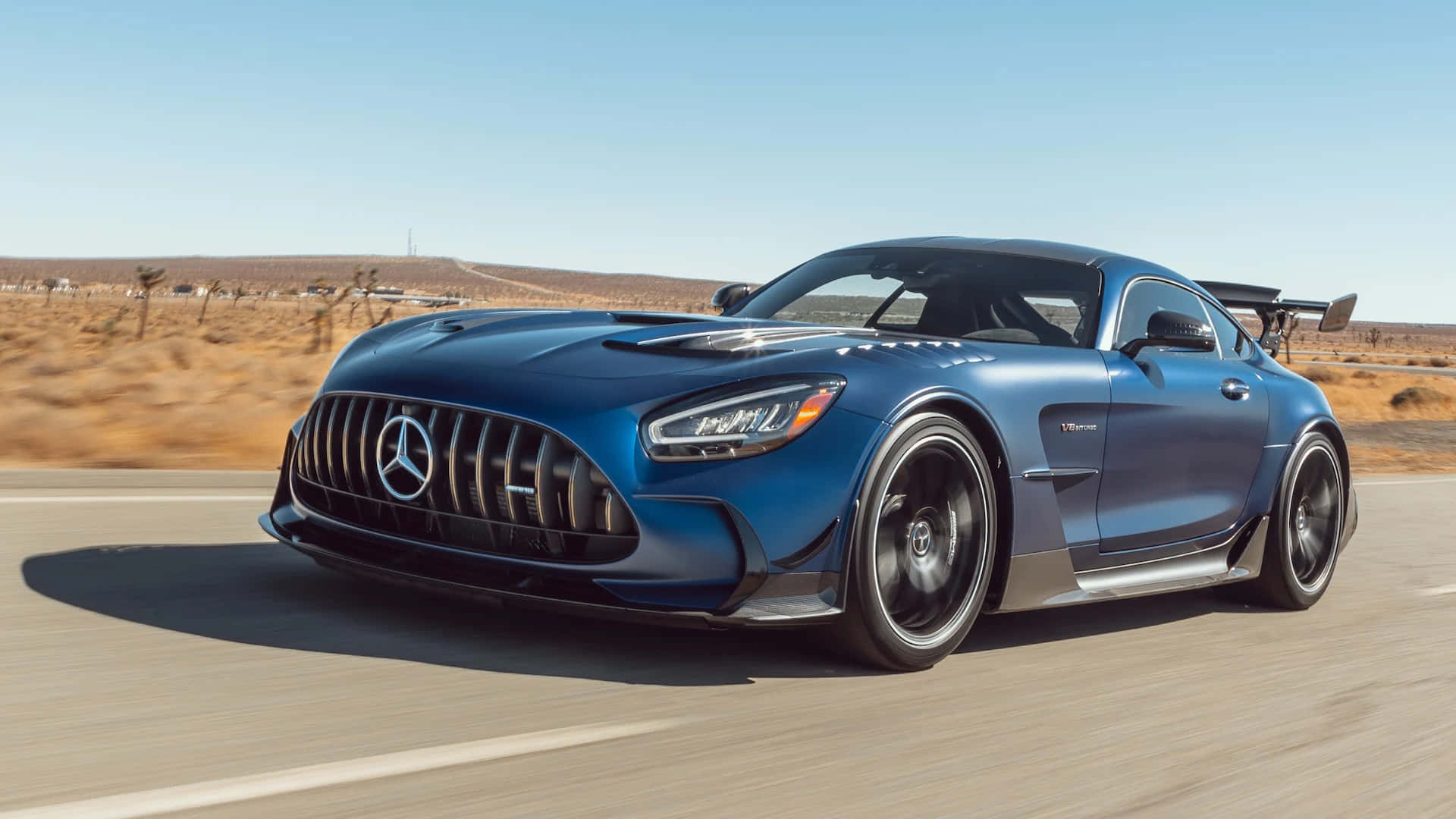 Mercedes Benz Amg Gt 桌布 壁紙 — 一架流線型的藍色 Mercedes-AMG GT R 賽車在晴朗的藍天下沿沙漠高速公路飛馳。