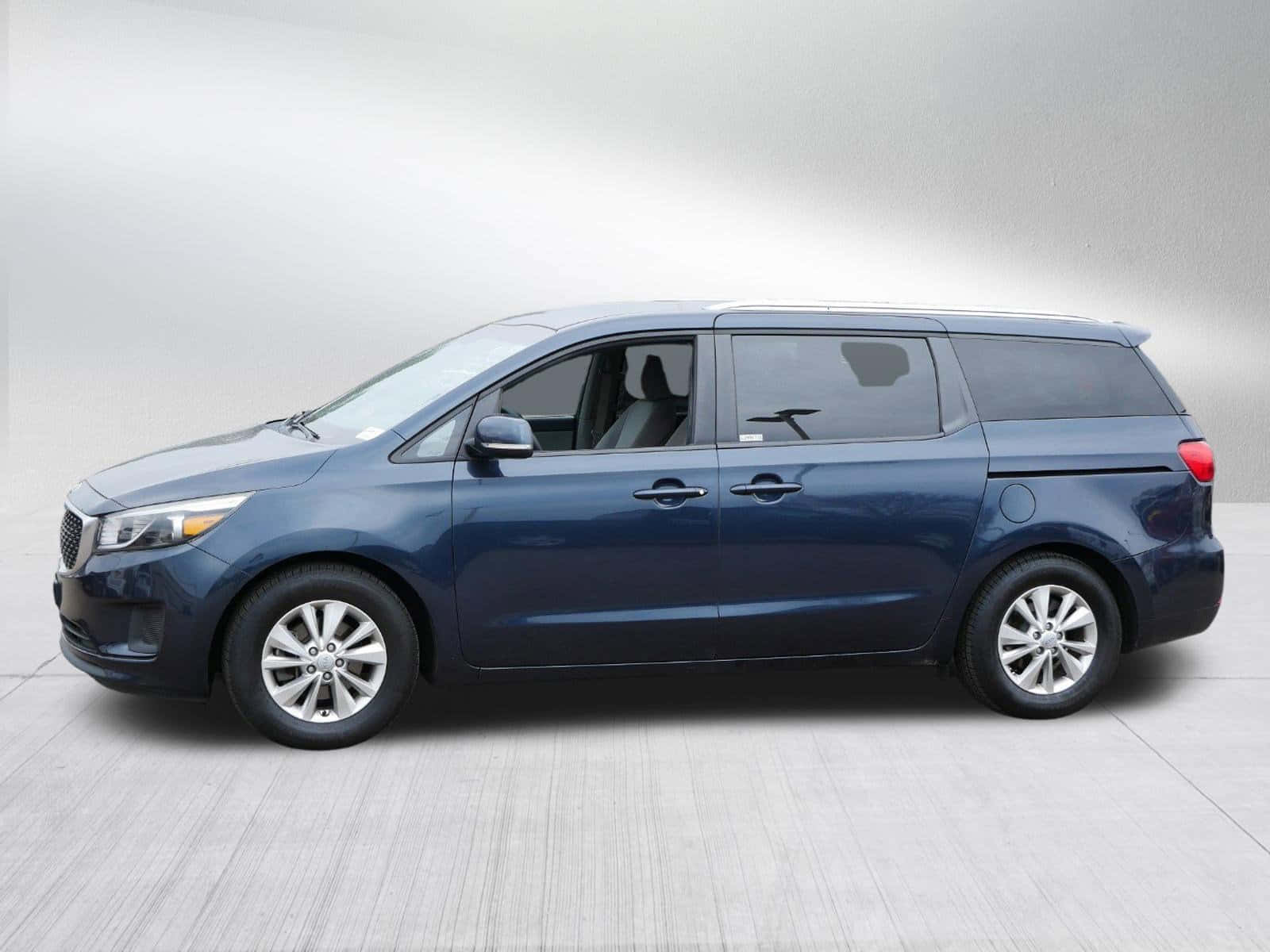 Kia Sedona 桌布 壁紙 — 一輛時尚的藍色小型貨車在柔和燈光下以側面輪廓展示於中性工作室背景前。