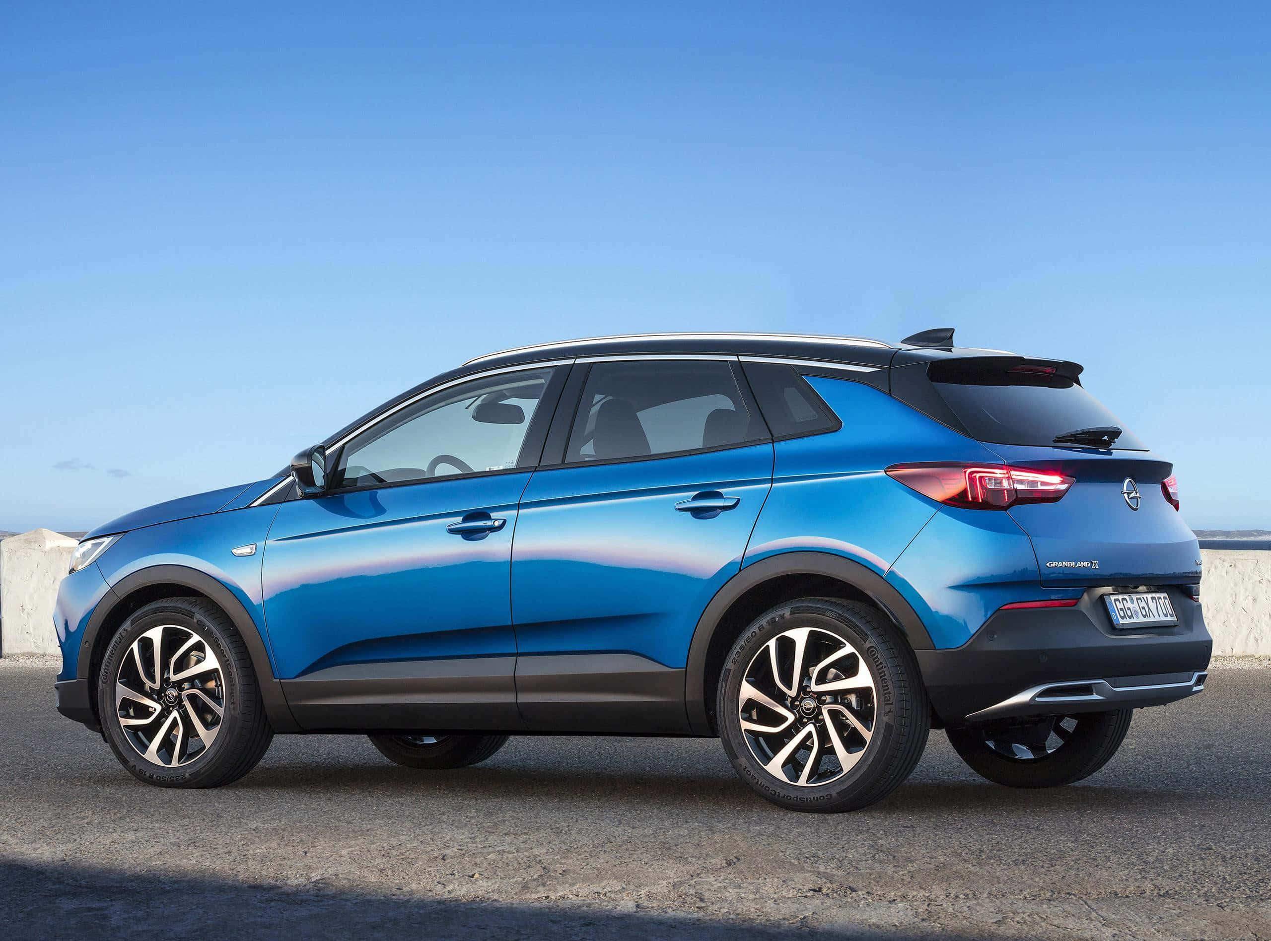 Opel Grandland X 桌布 壁紙 — 一輛時尚的藍色歐寶 Grandland X SUV 停在瀝青路面上，背景是晴朗的藍天和混凝土牆。