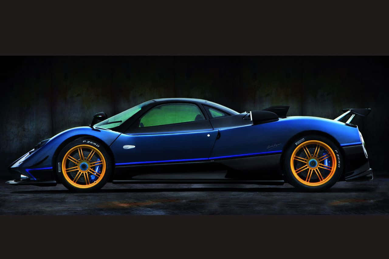Pagani Zonda Tricolore 桌布 壁紙 — 一輛時尚的藍色帕加尼超跑，配備金色輪圈和發光飾件，在黑暗的攝影棚中靠著紋理牆壁停放。