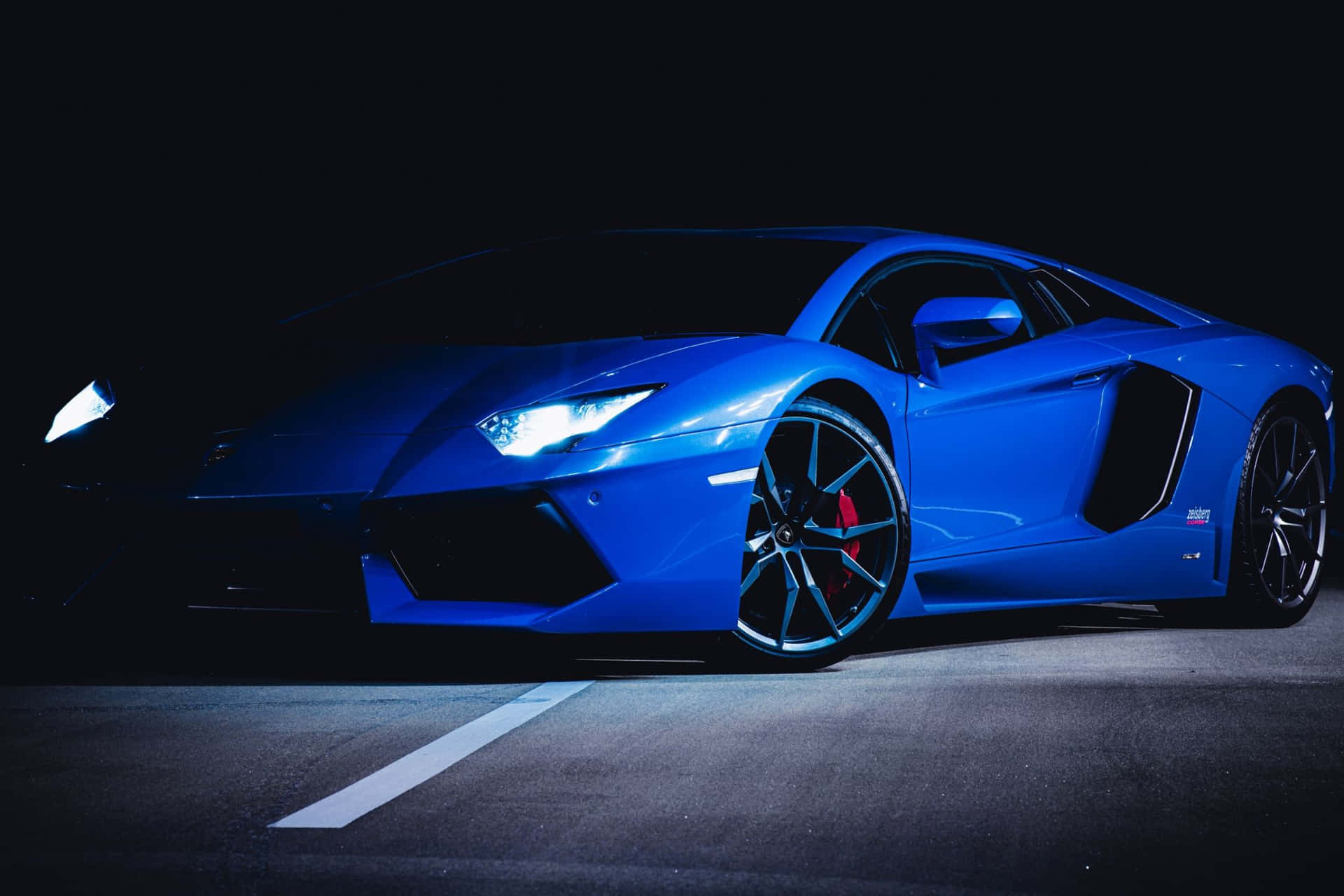  壁紙 — 一輛時尚的藍色跑車在夜間聚光燈下閃耀，在瀝青路面上呈現銳利線條和發光車頭燈。